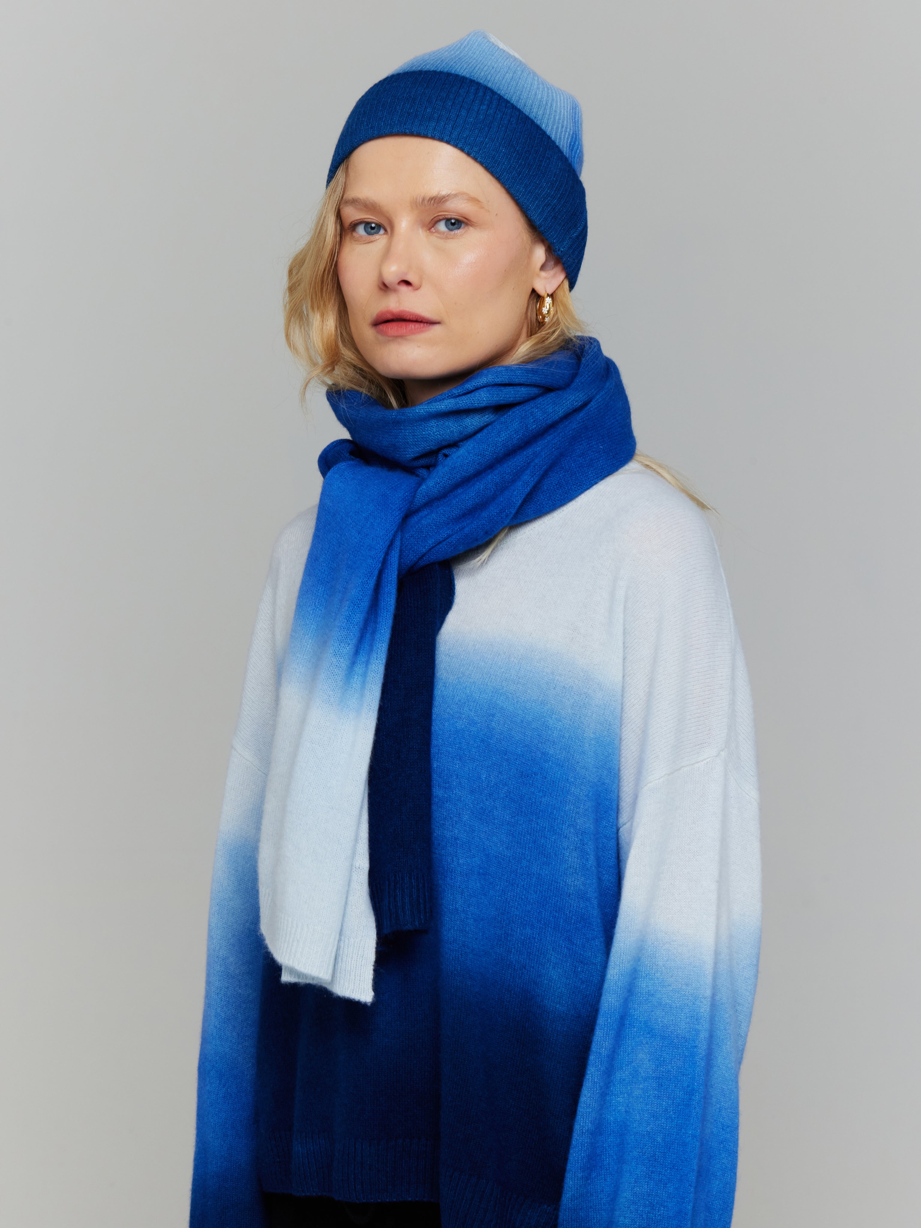 A person wearing a blue and white ombre beanie hat and matching scarf