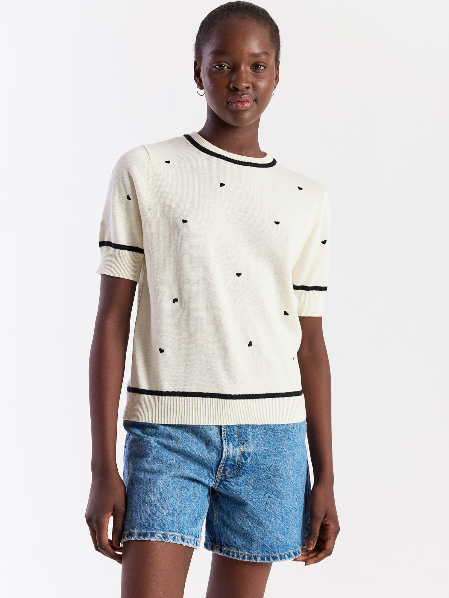 Woman wearing a cream sweater with black polka dots and denim shorts on a white background