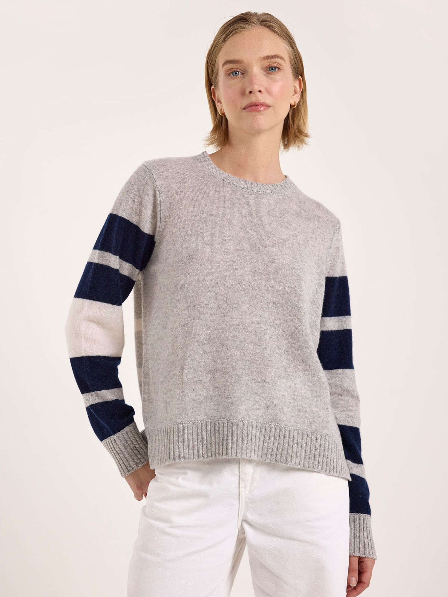 Woman wearing a gray cashmere sweater with blue and white striped sleeves on a white background