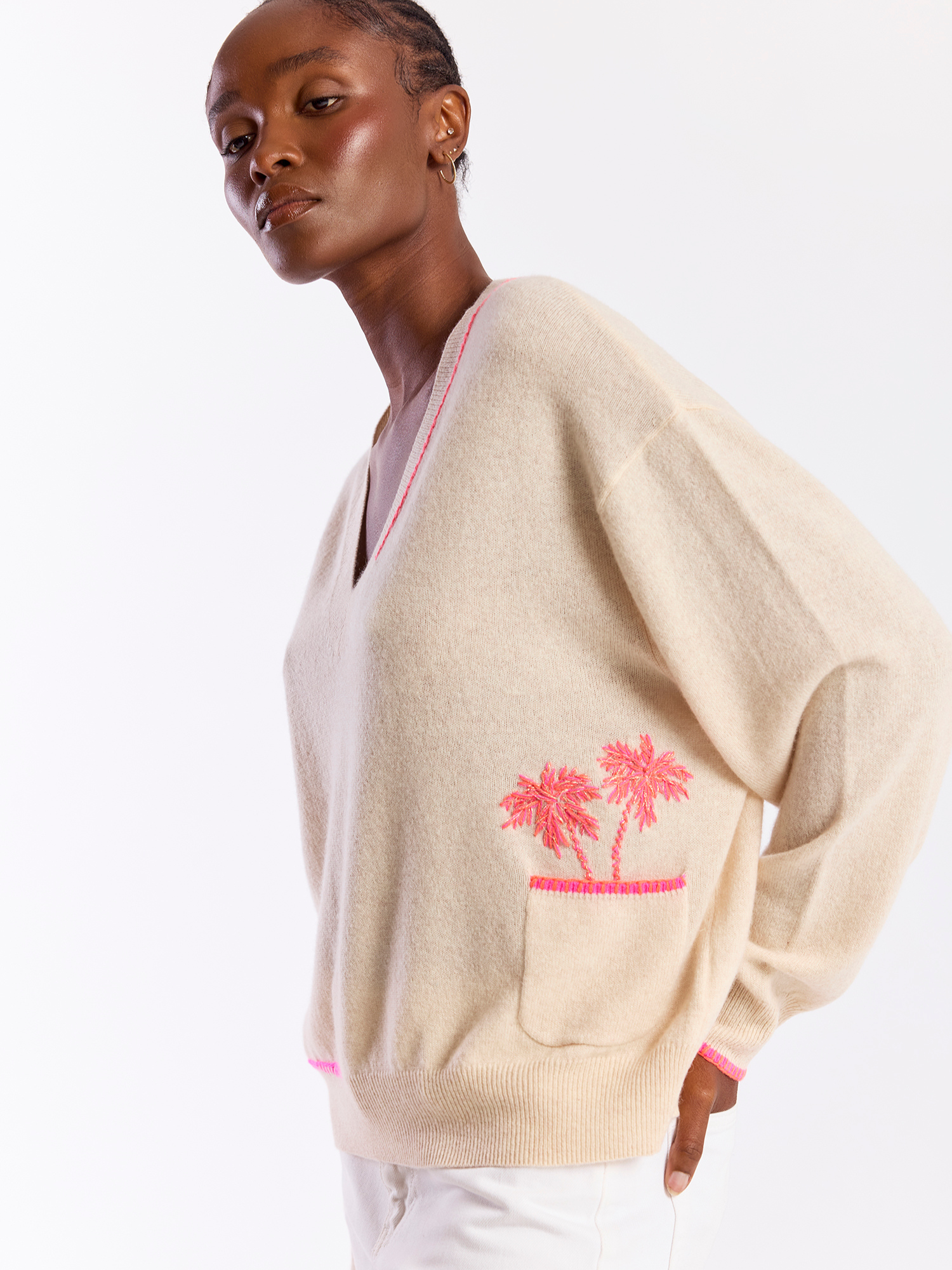 Woman wearing a beige cardigan with pink palm tree design on a white background