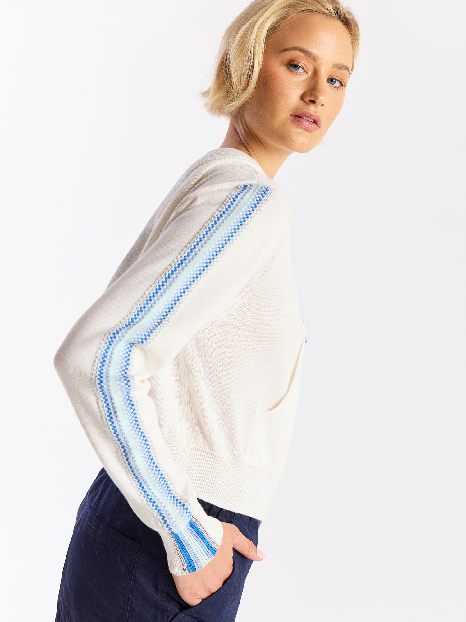 Woman wearing a white sweater with blue accents on a plain background