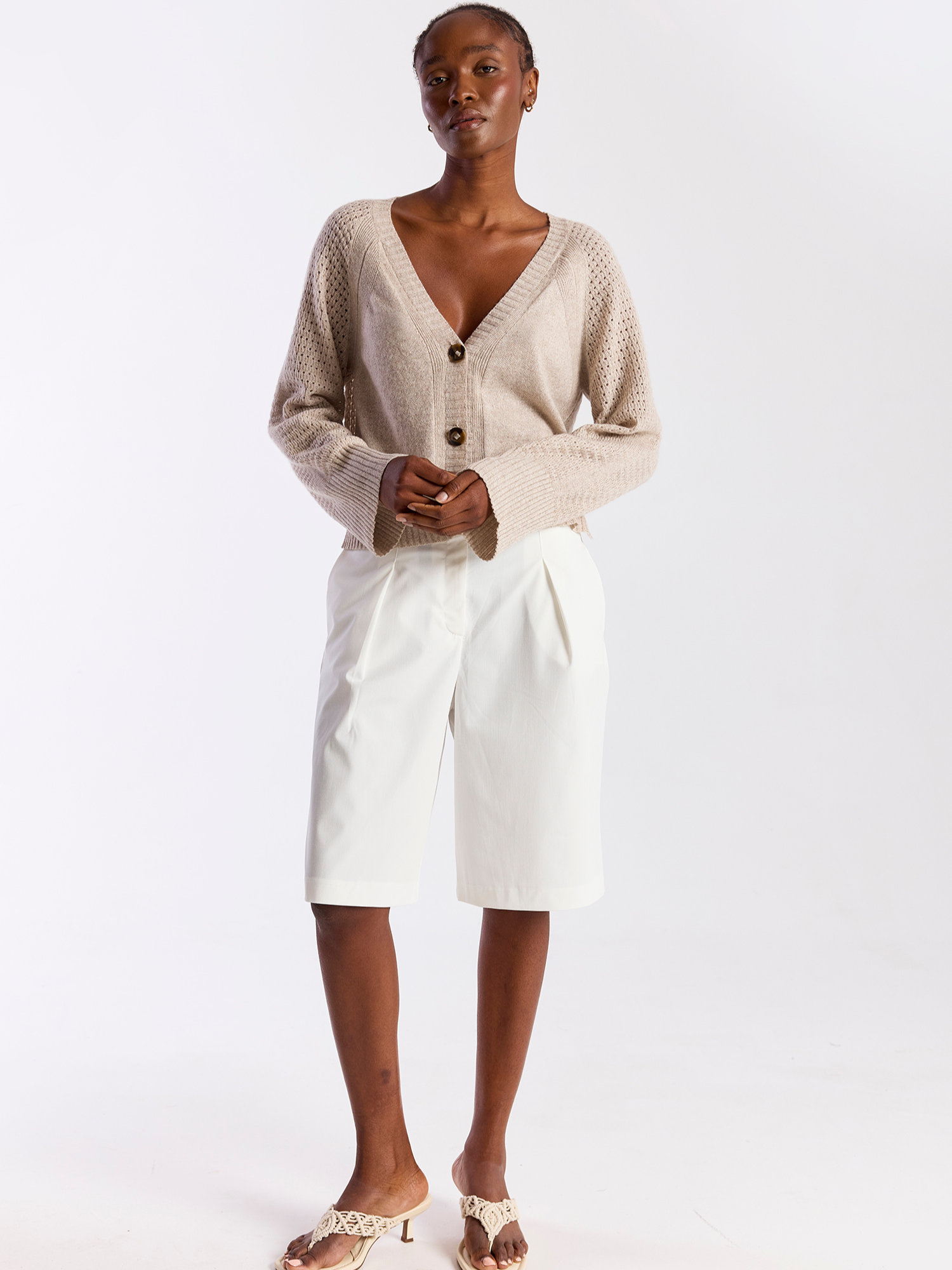 Woman wearing a beige cardigan and white skirt on a plain background