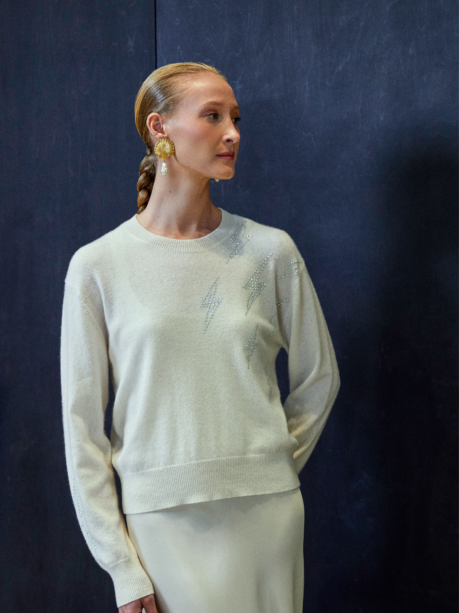 Woman wearing a light-colored sweater with subtle patterns against a dark background