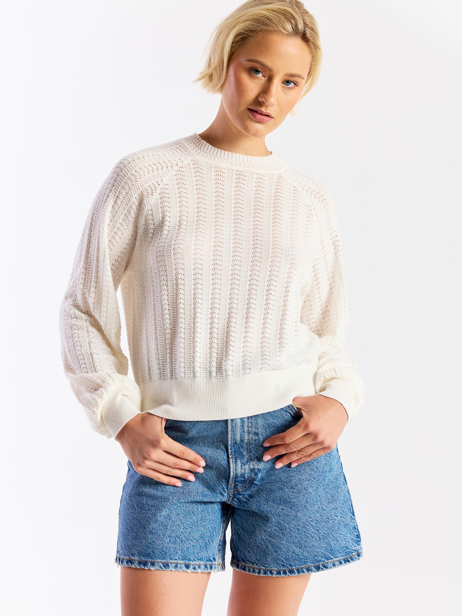 Woman wearing a white sweater and blue denim shorts on a white background