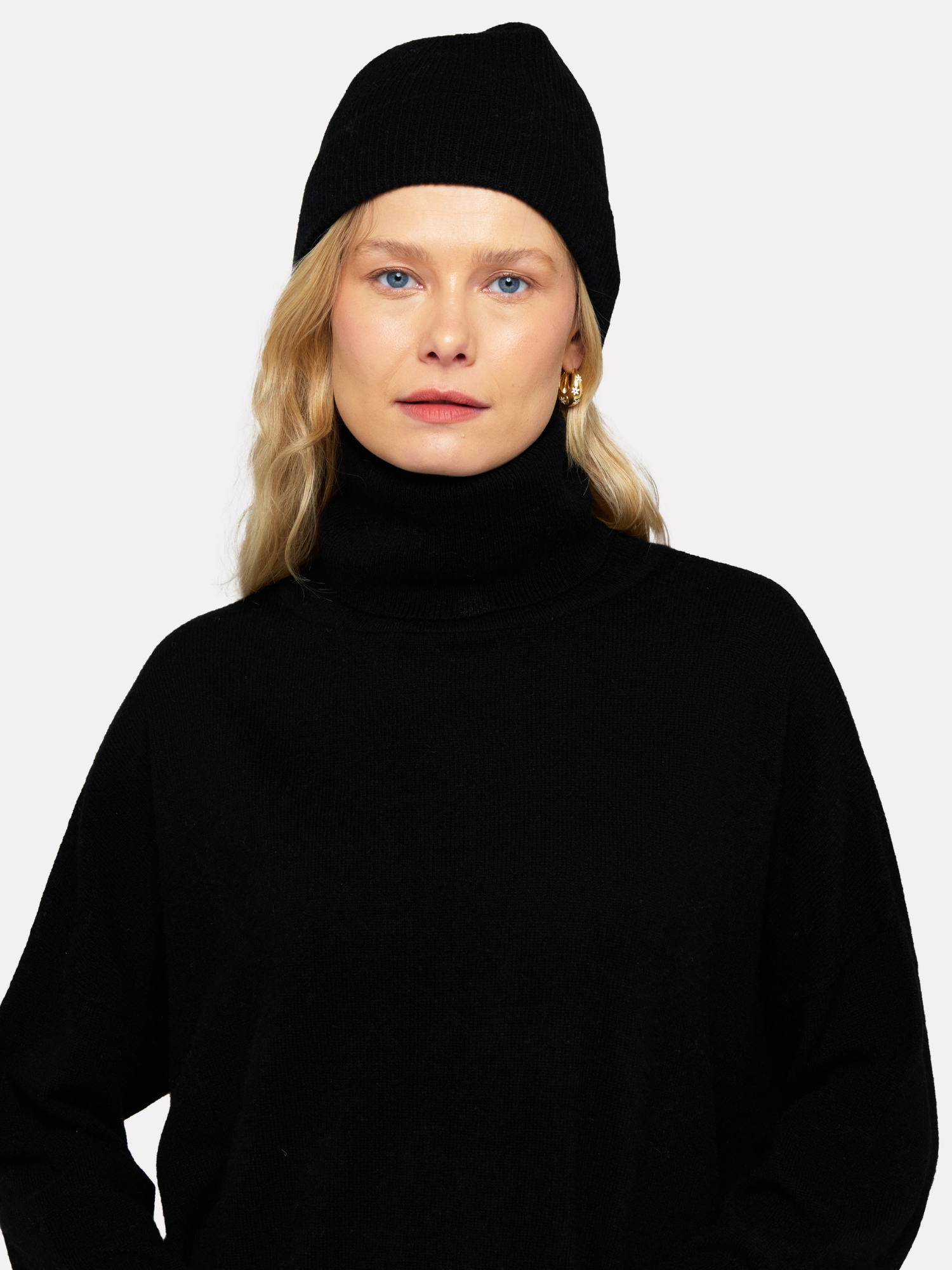 Person wearing a black turtleneck and black beanie against a white background