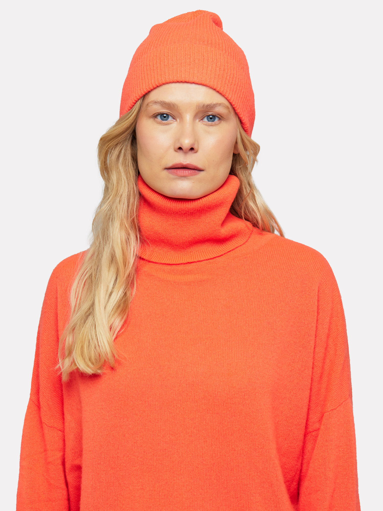 Person wearing an orange outfit with a matching beanie on a white background