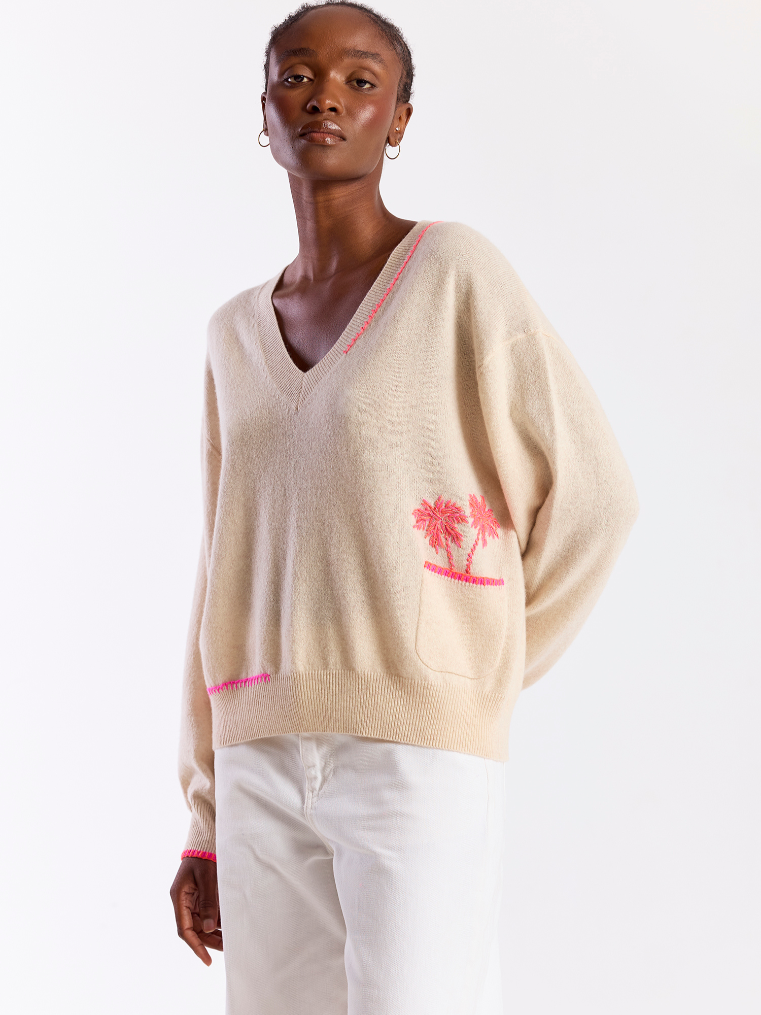 Woman wearing a beige sweater with pink accents and a palm tree design on a white background