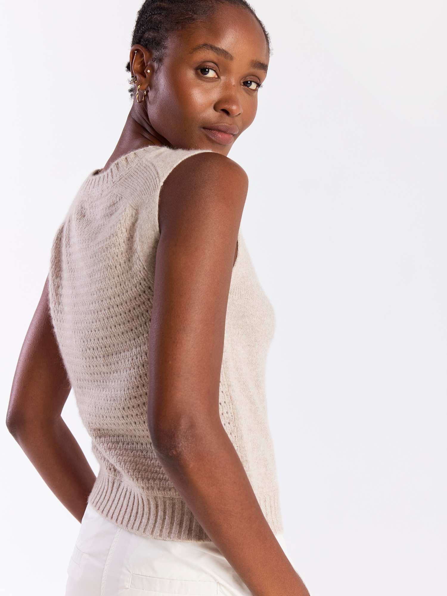 Woman wearing a beige sleeveless knitted top against a white background