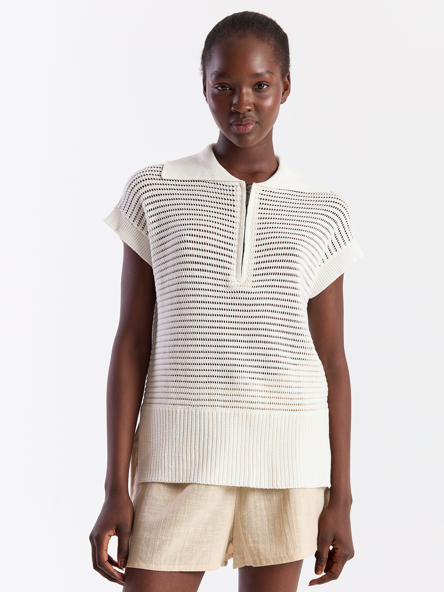 Woman wearing a white knit top and beige shorts on a white background