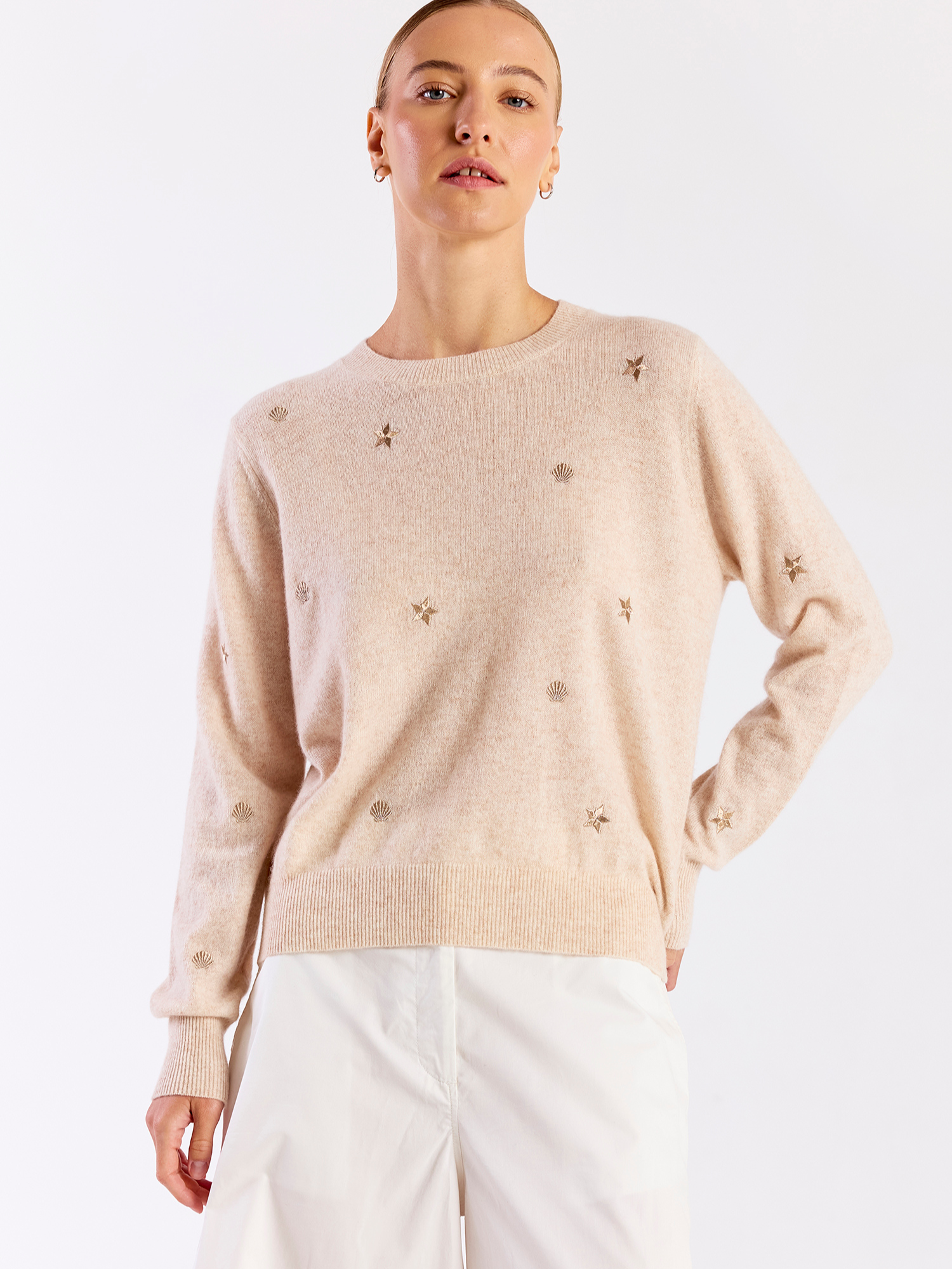 Woman wearing a beige sweater with small decorative elements on a white background