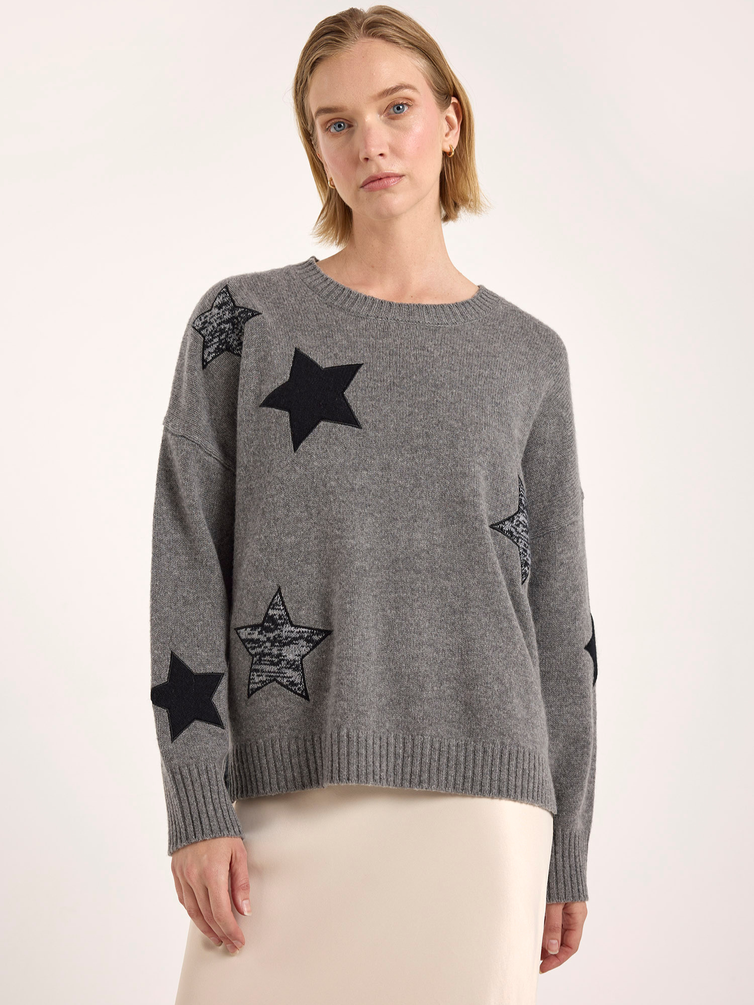 Woman wearing a gray sweater with black star patterns on a white background