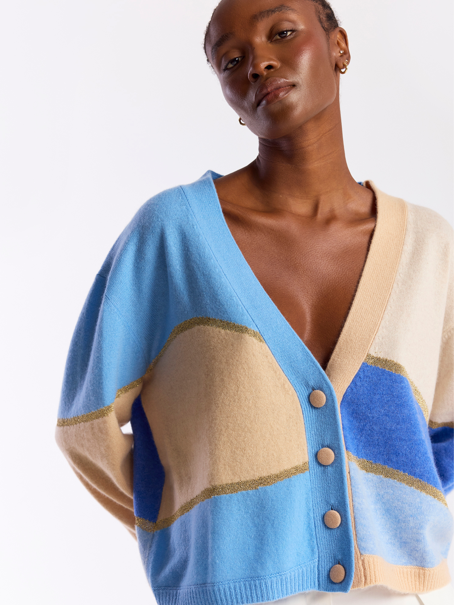 Woman wearing a blue and beige cashmere cardigan with button details on a white background