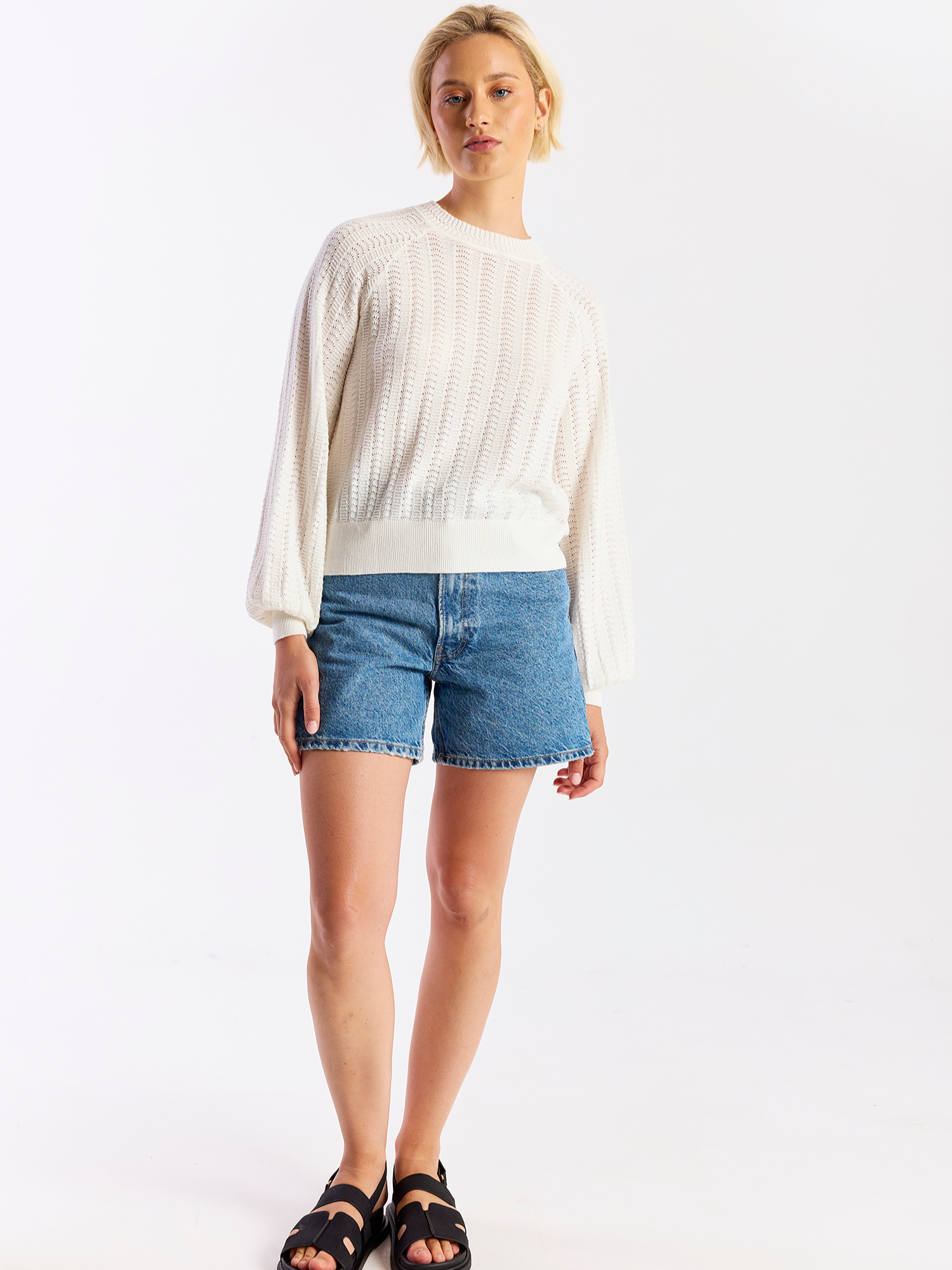 Woman wearing a white sweater and blue denim shorts on a white background