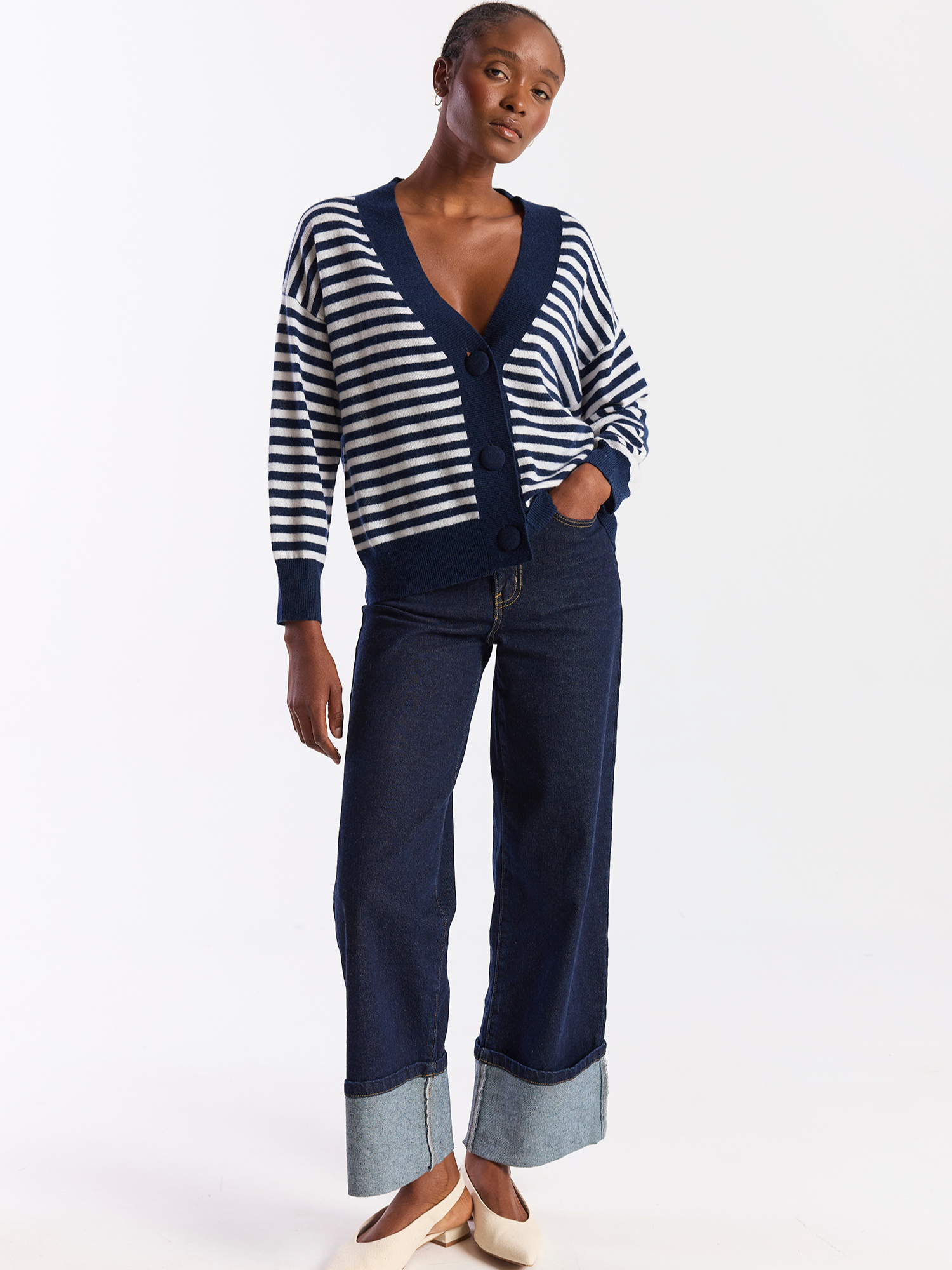 Person wearing a blue and white striped sweater with a navy cardigan and pants on a white background