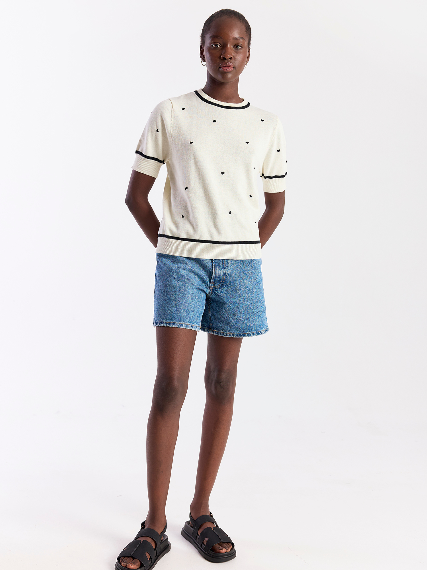 Person wearing a white t-shirt with black trim and denim shorts on a white background