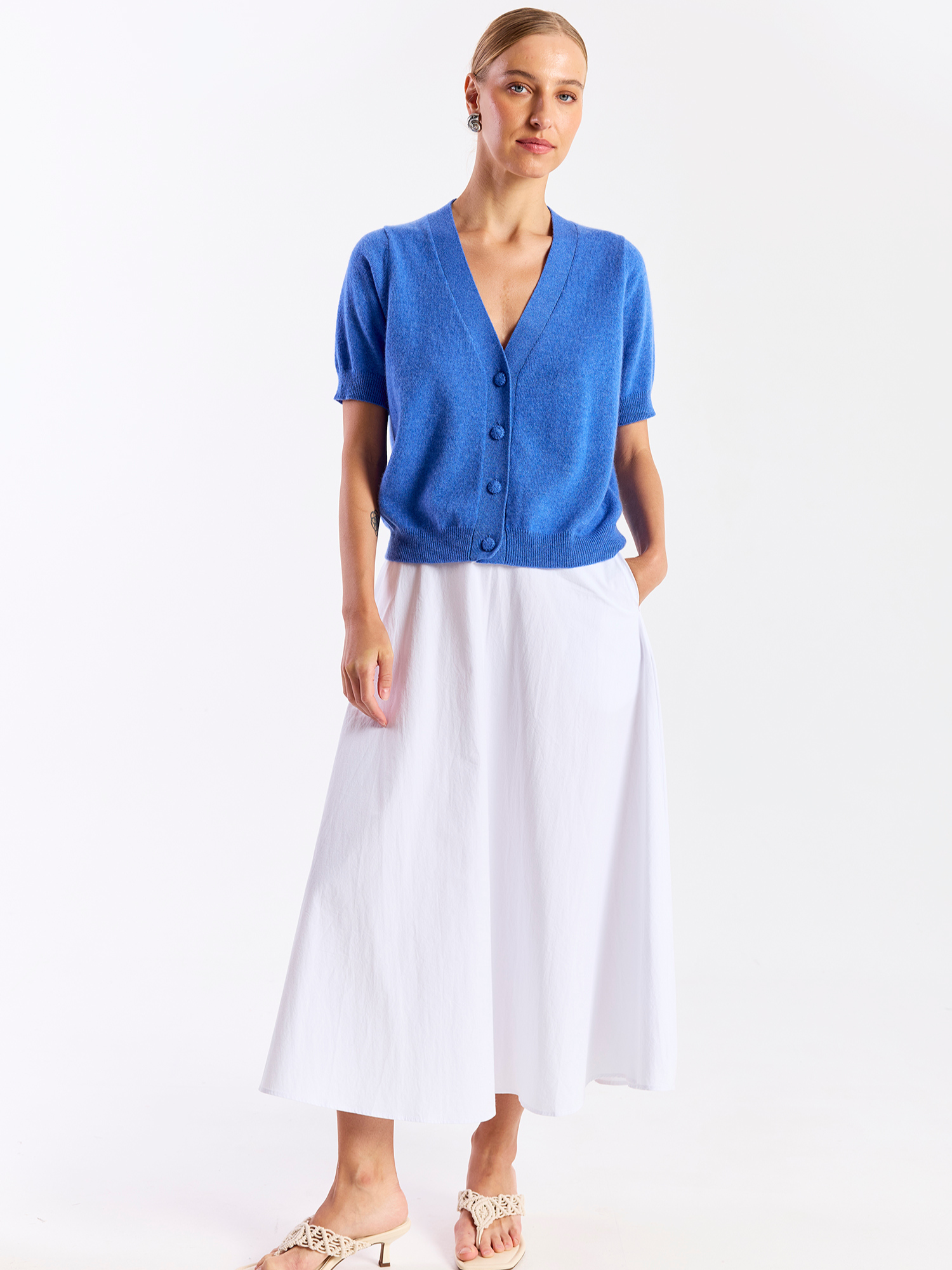 Woman wearing a blue cardigan and white skirt on a white background