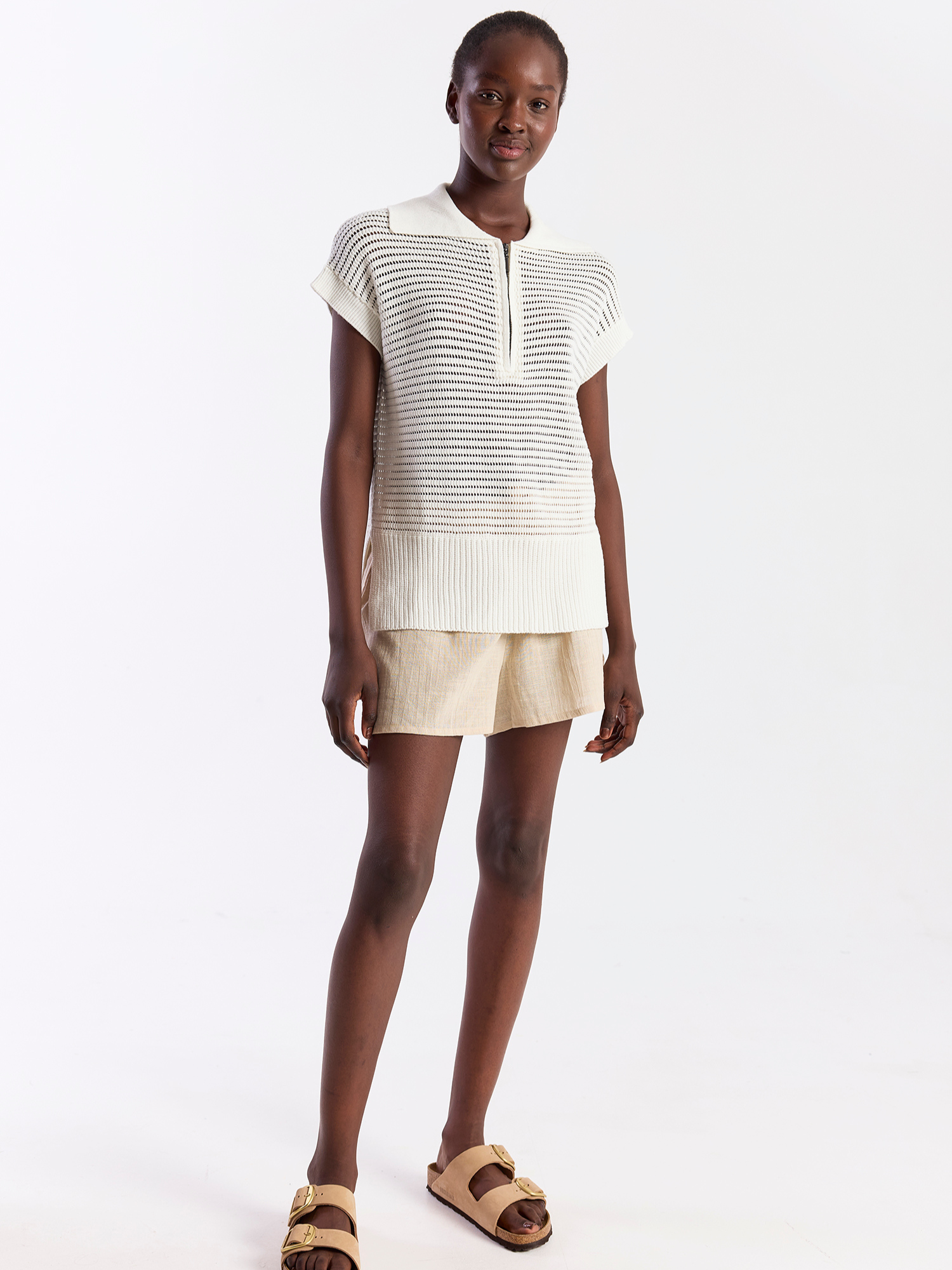 Woman wearing a white and black striped top with beige shorts on a white background