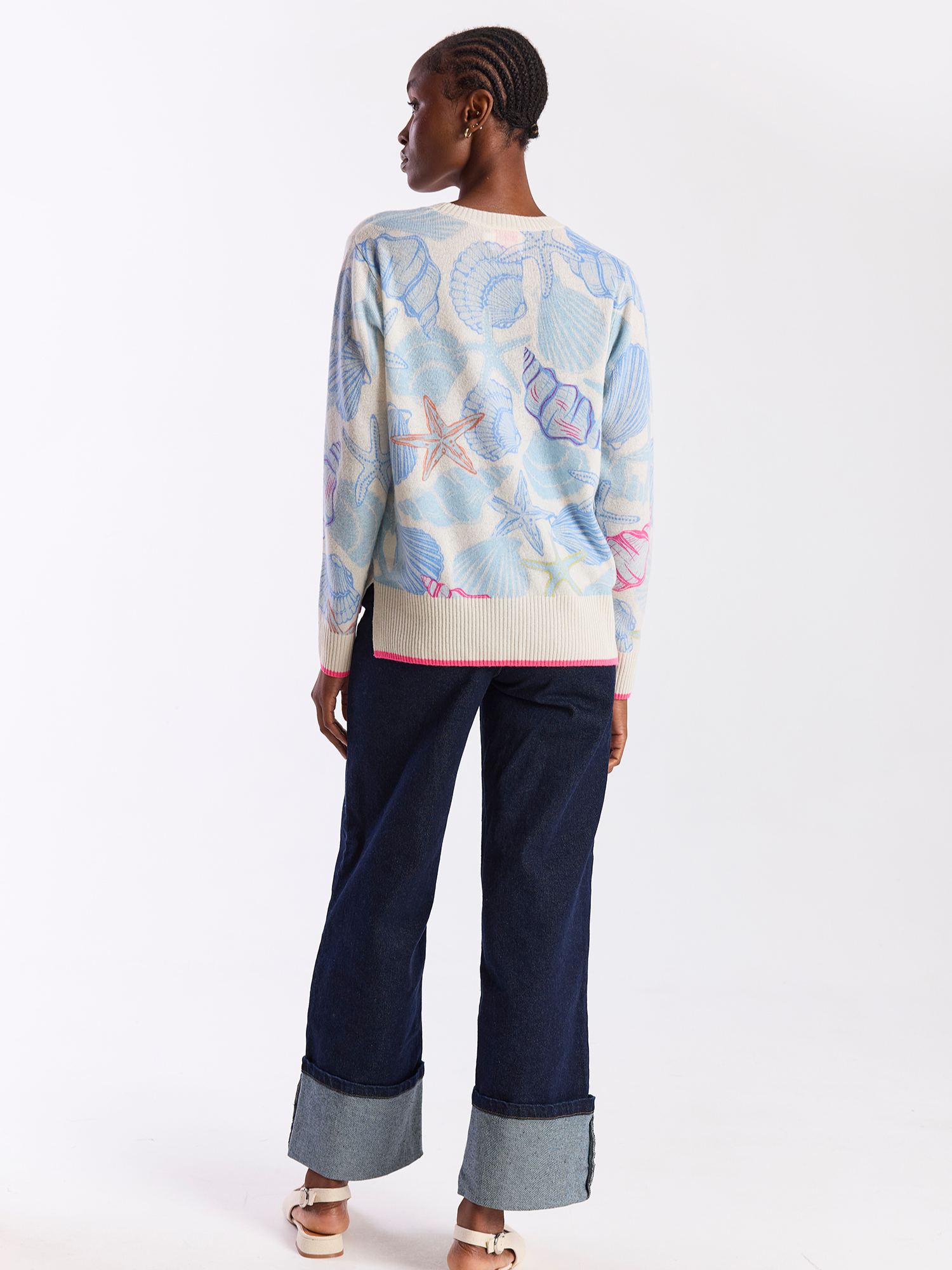 Person wearing a patterned sweater and dark pants on a white background