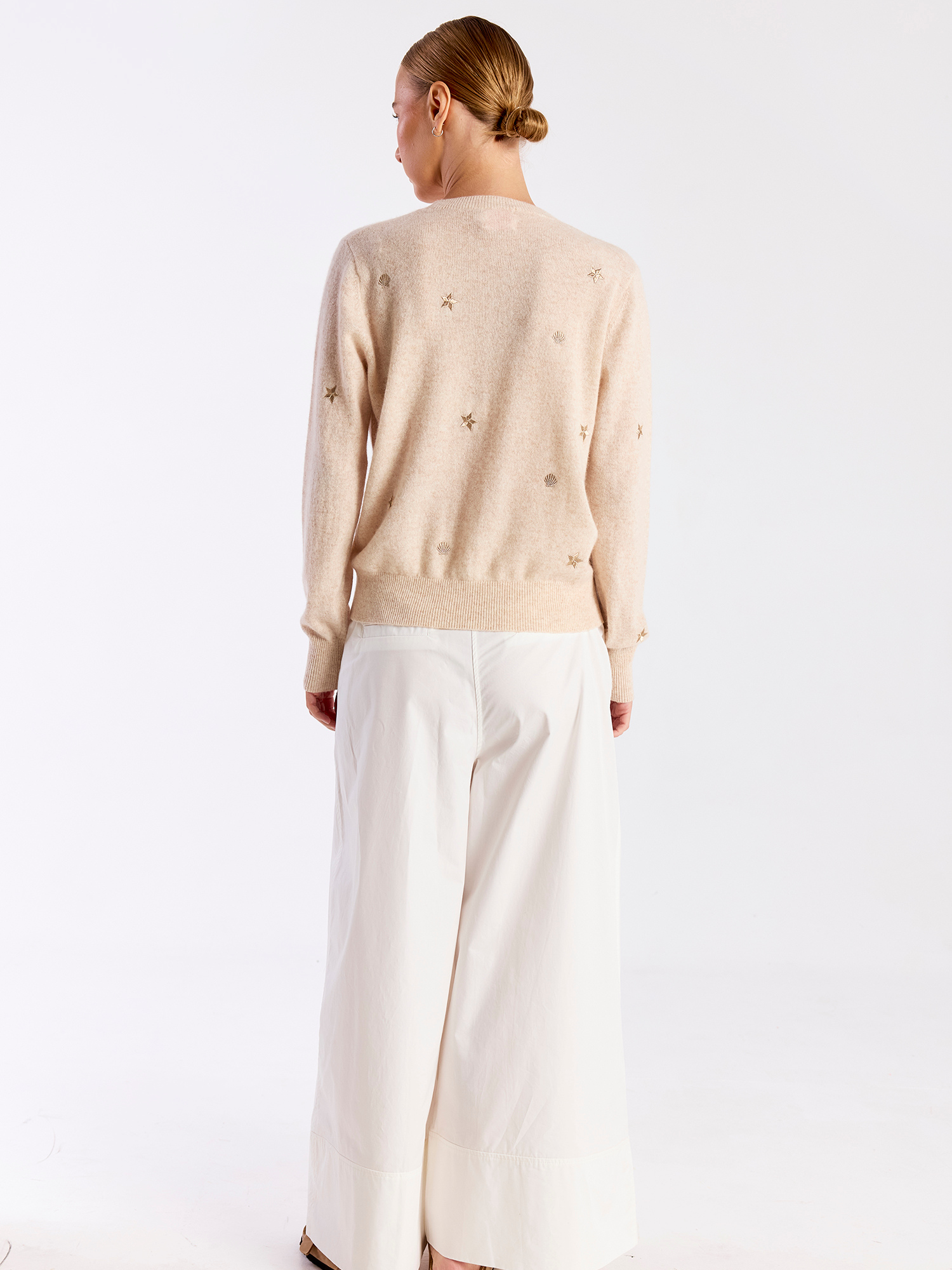 Person wearing a beige sweater with subtle patterns and white pants on a light background
