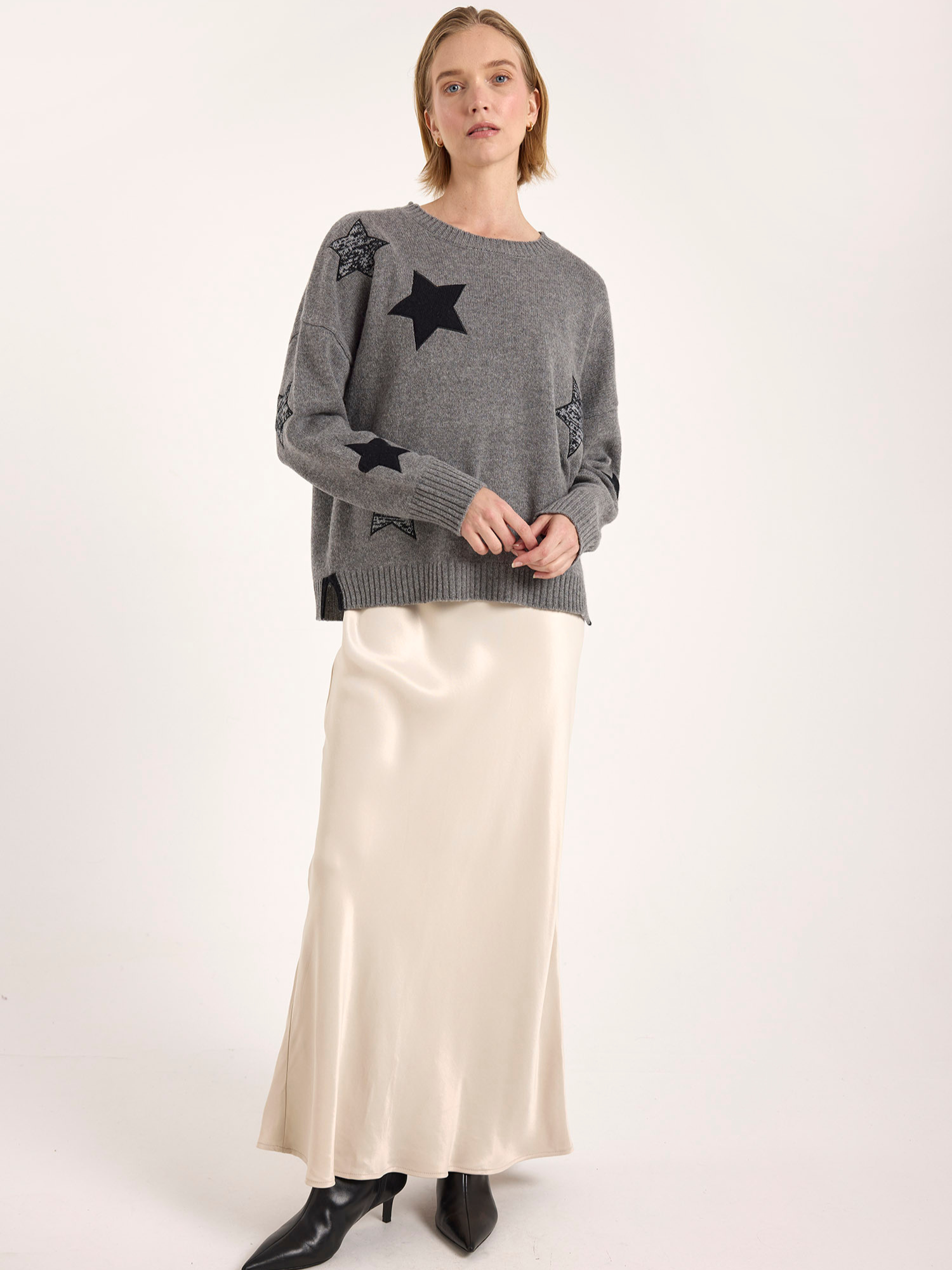 Woman wearing a gray sweater with star patterns and a white skirt on a white background
