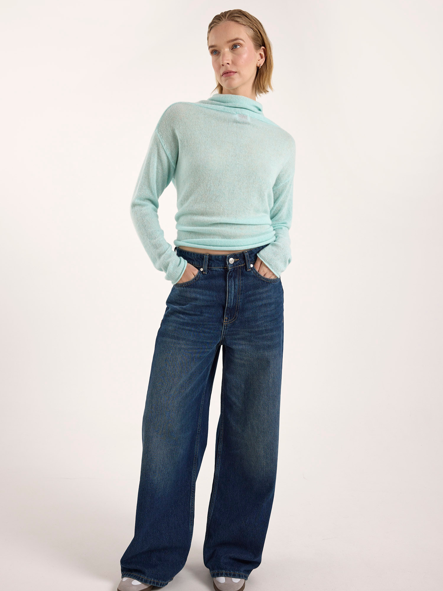 Woman wearing a light blue sweater and dark blue jeans on a white background