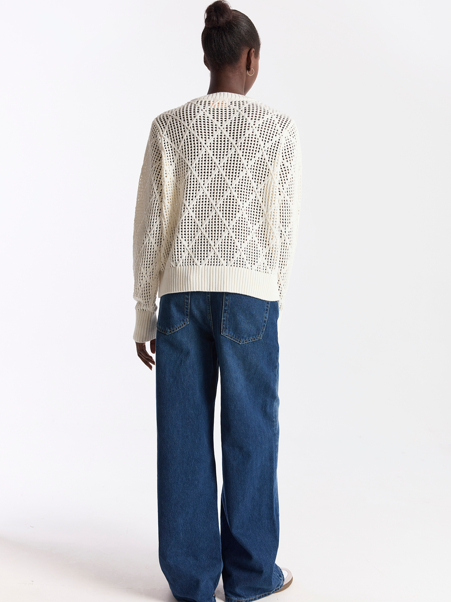 Person wearing a white textured sweater and blue jeans on a white background