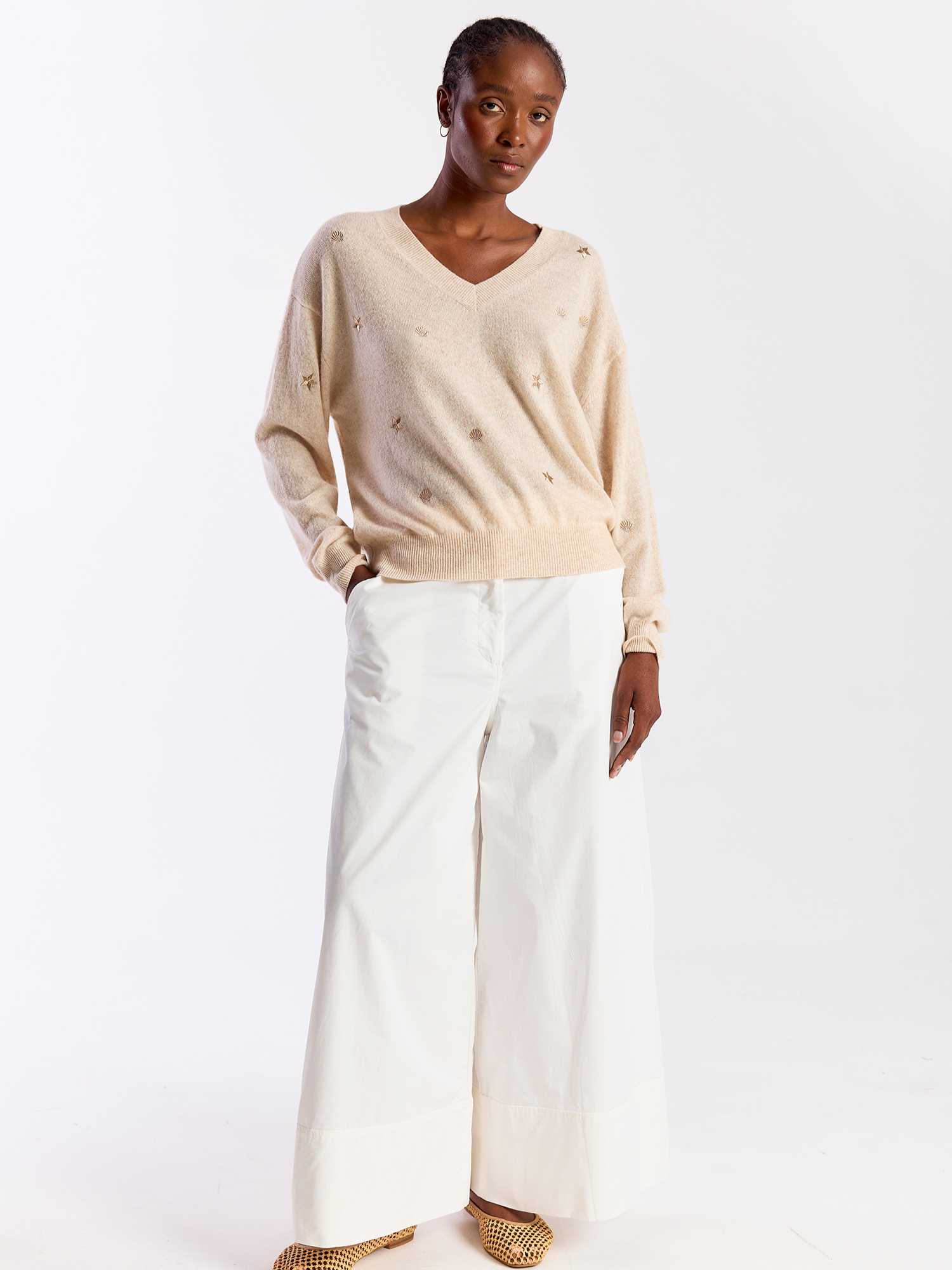 Woman wearing a beige sweater and white pants on a white background
