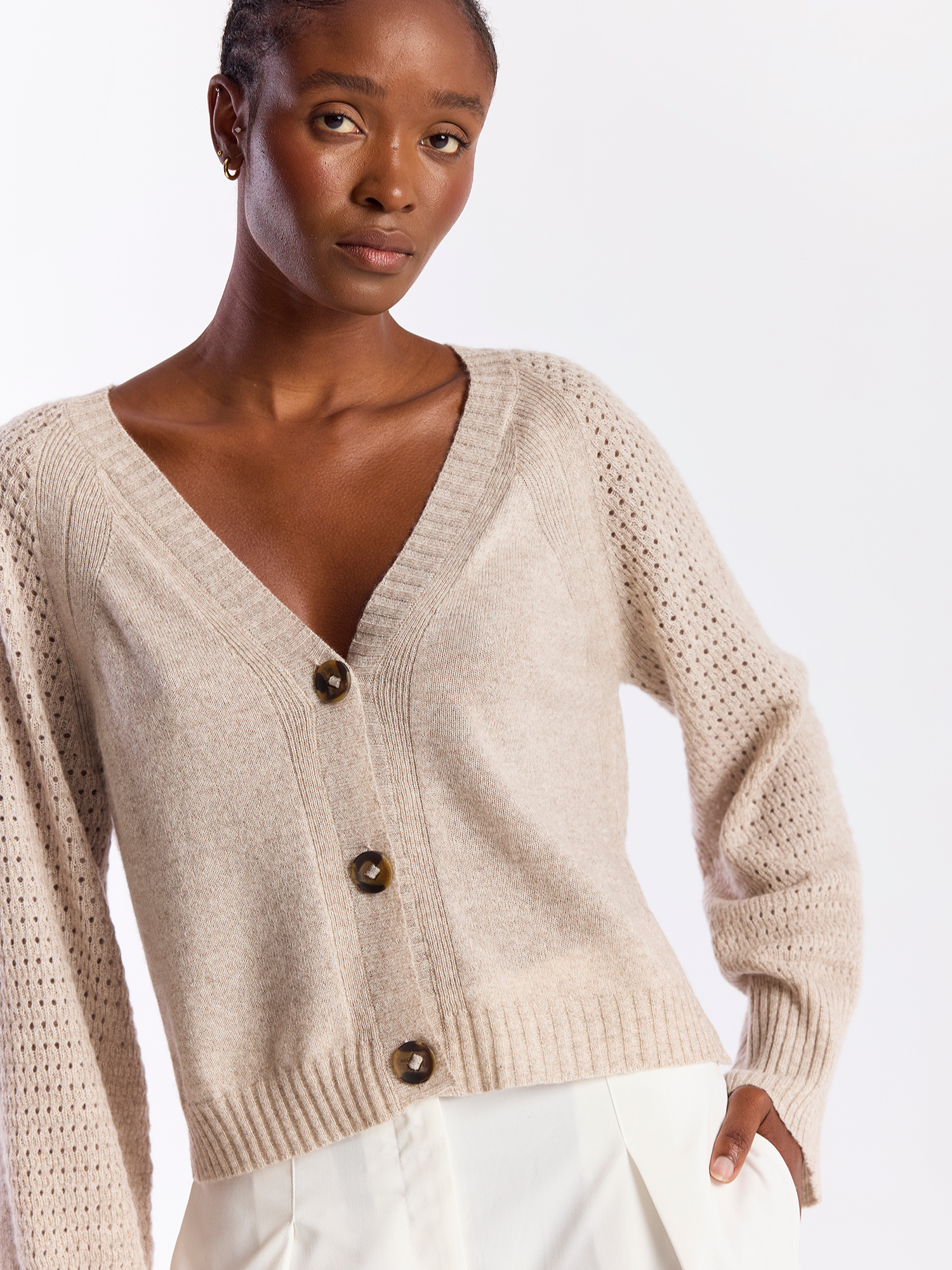 Woman wearing a beige knitted cardigan with brown buttons on a white background