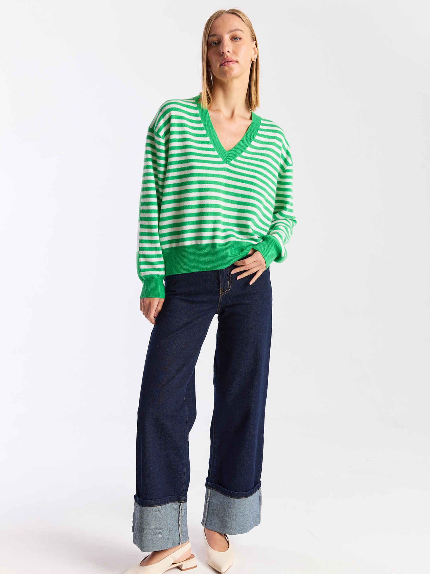 Woman wearing a green and white striped sweater and dark blue jeans on a white background
