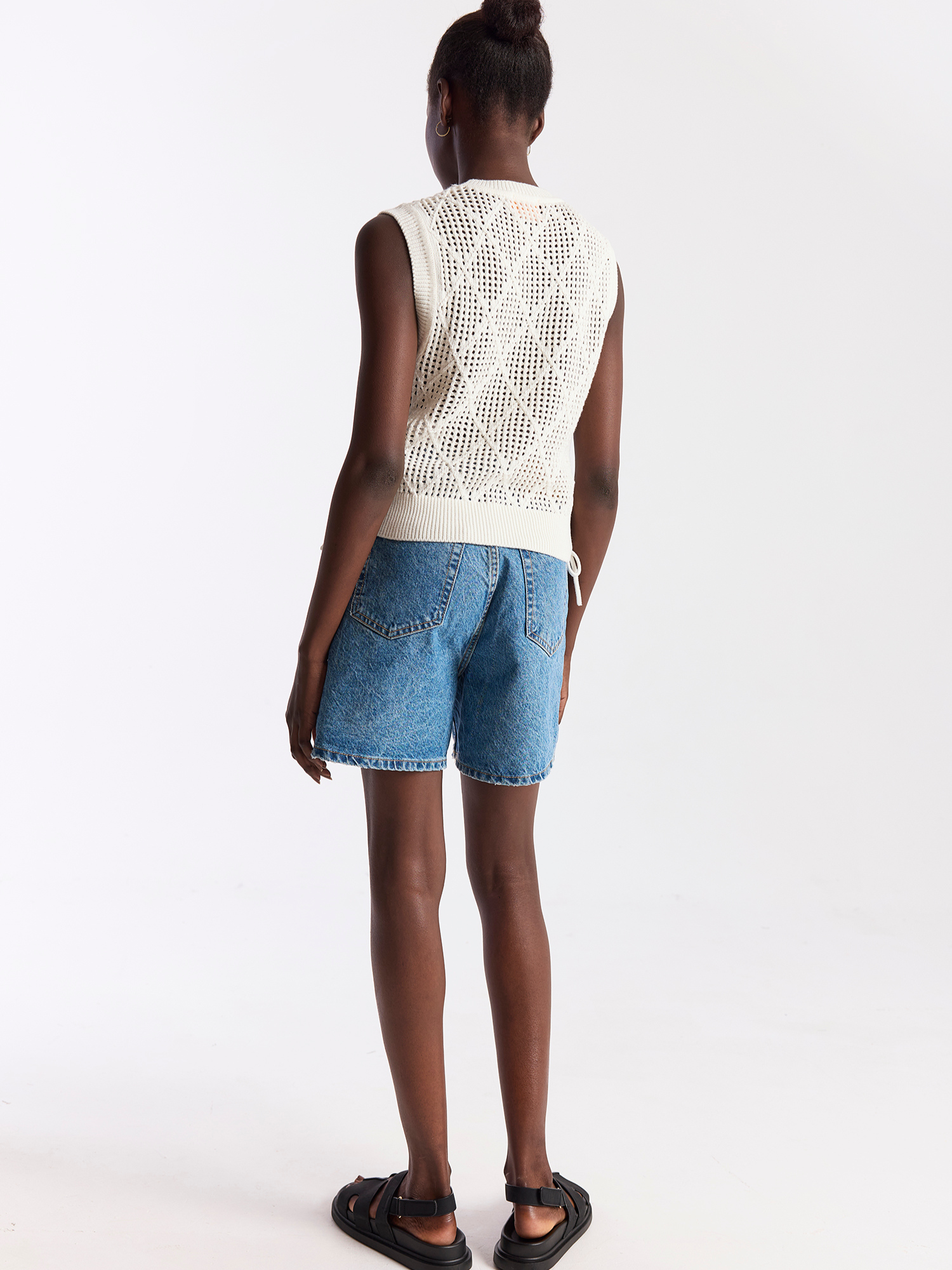 Person wearing a white sleeveless top and blue denim shorts on a white background
