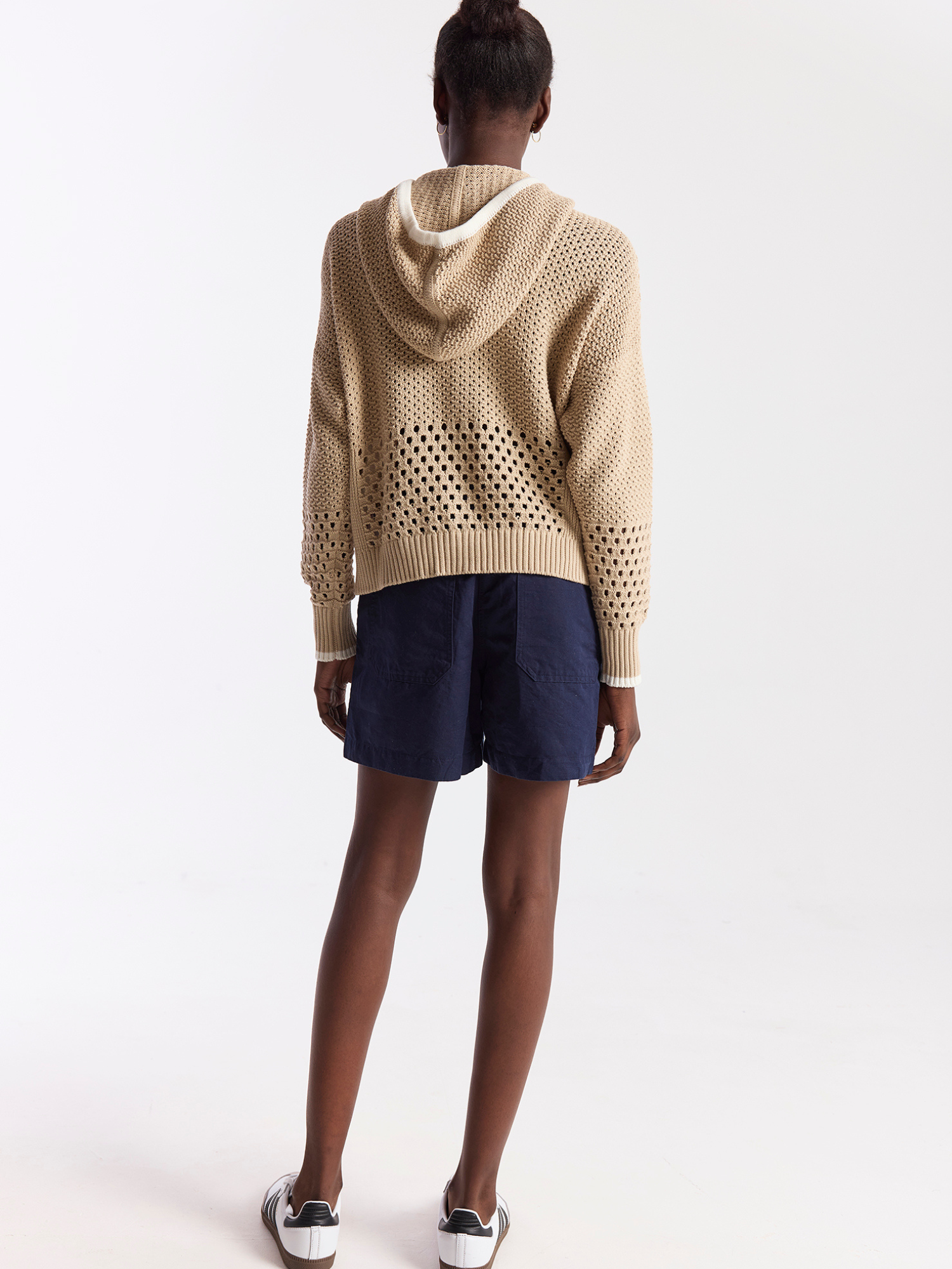 Person wearing a beige knitted hoodie with cut-out design on a white background