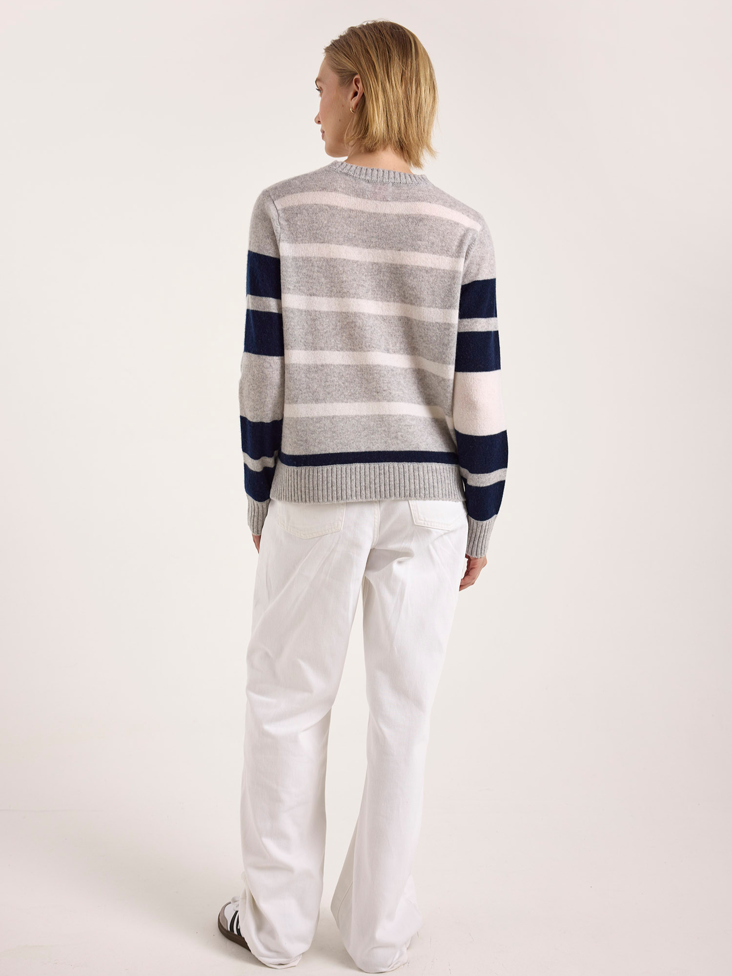 Person wearing a striped sweater and white pants on a plain background