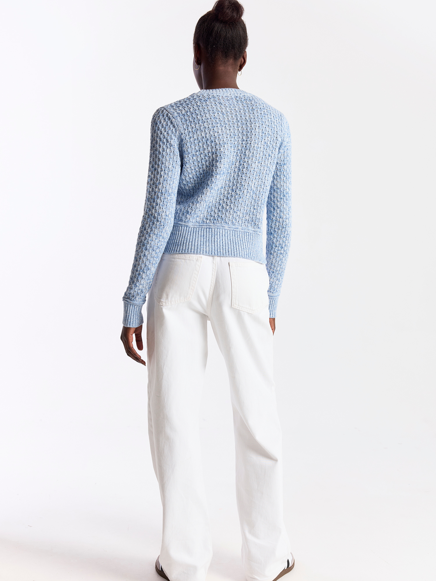 Person wearing a light blue textured sweater and white pants on a white background