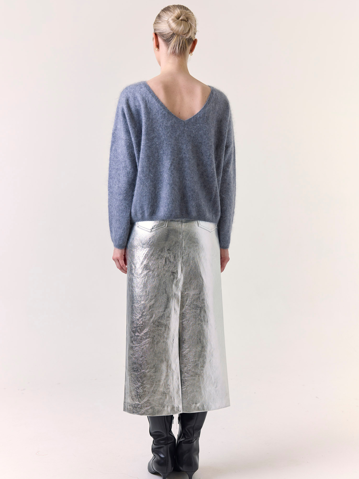Person wearing a blue sweater and silver skirt on a white background