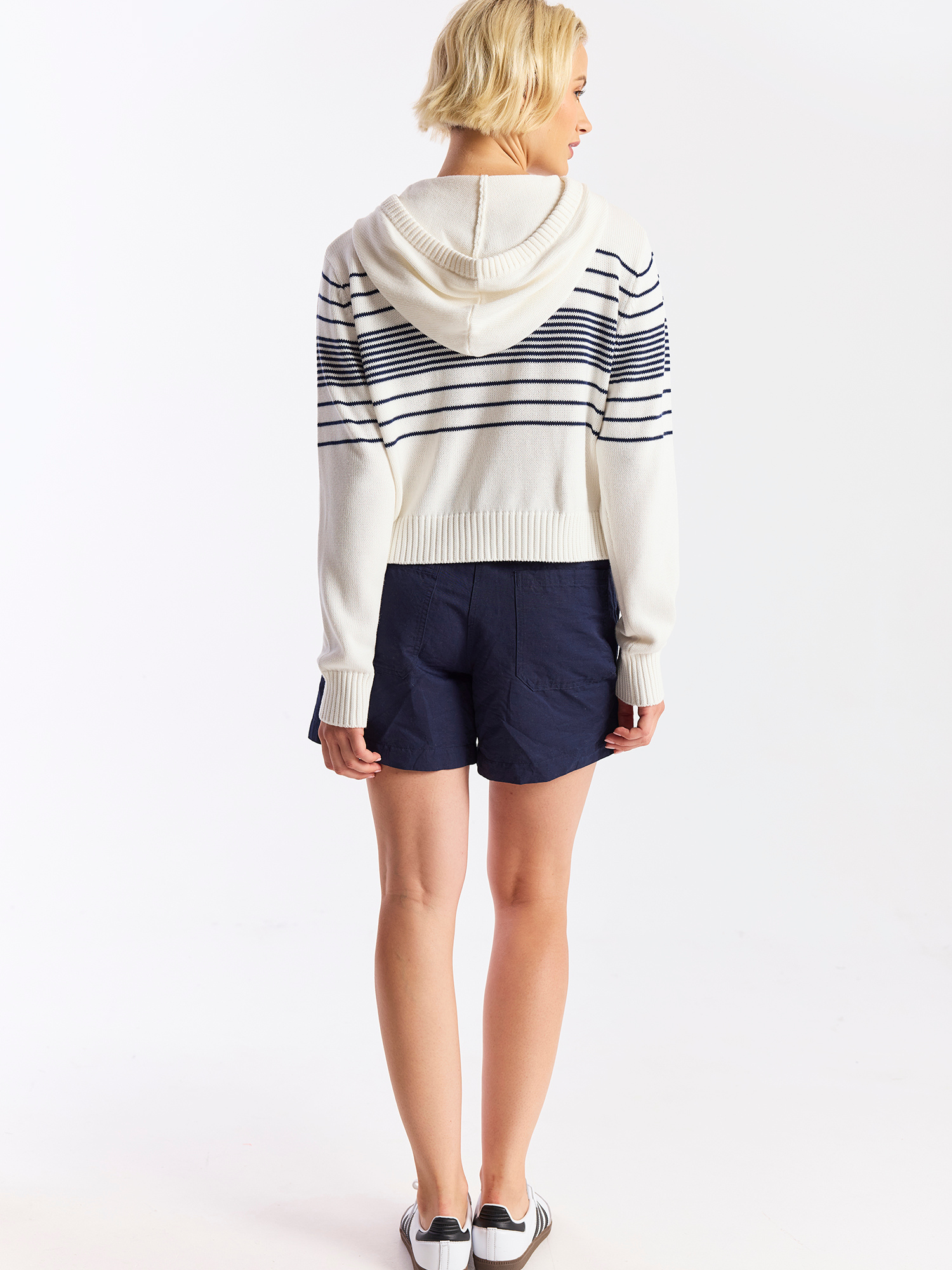 Person wearing a striped sweater and navy shorts on a white background