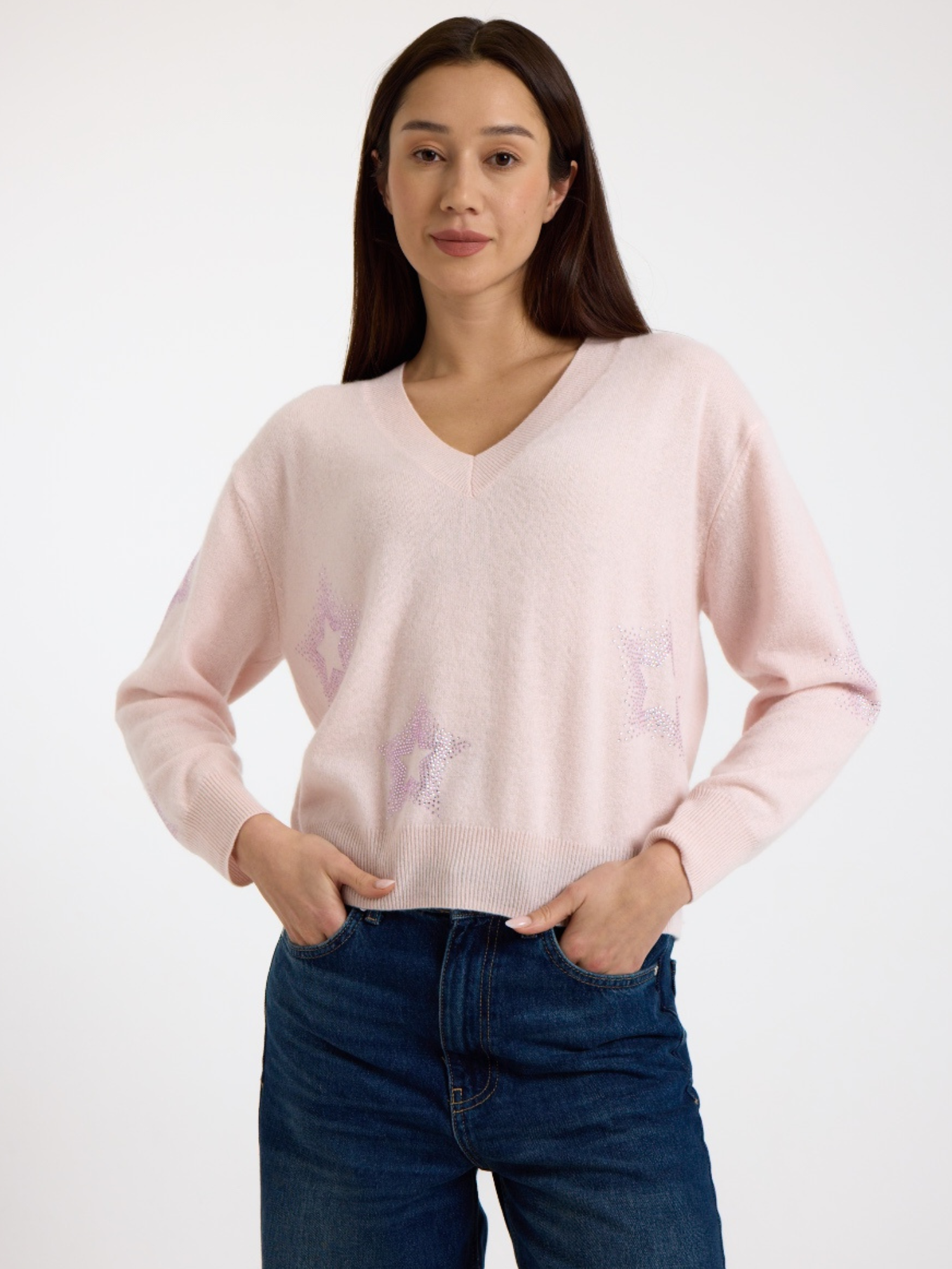 Woman wearing a light pink sweater with subtle star pattern and dark blue jeans on a white background