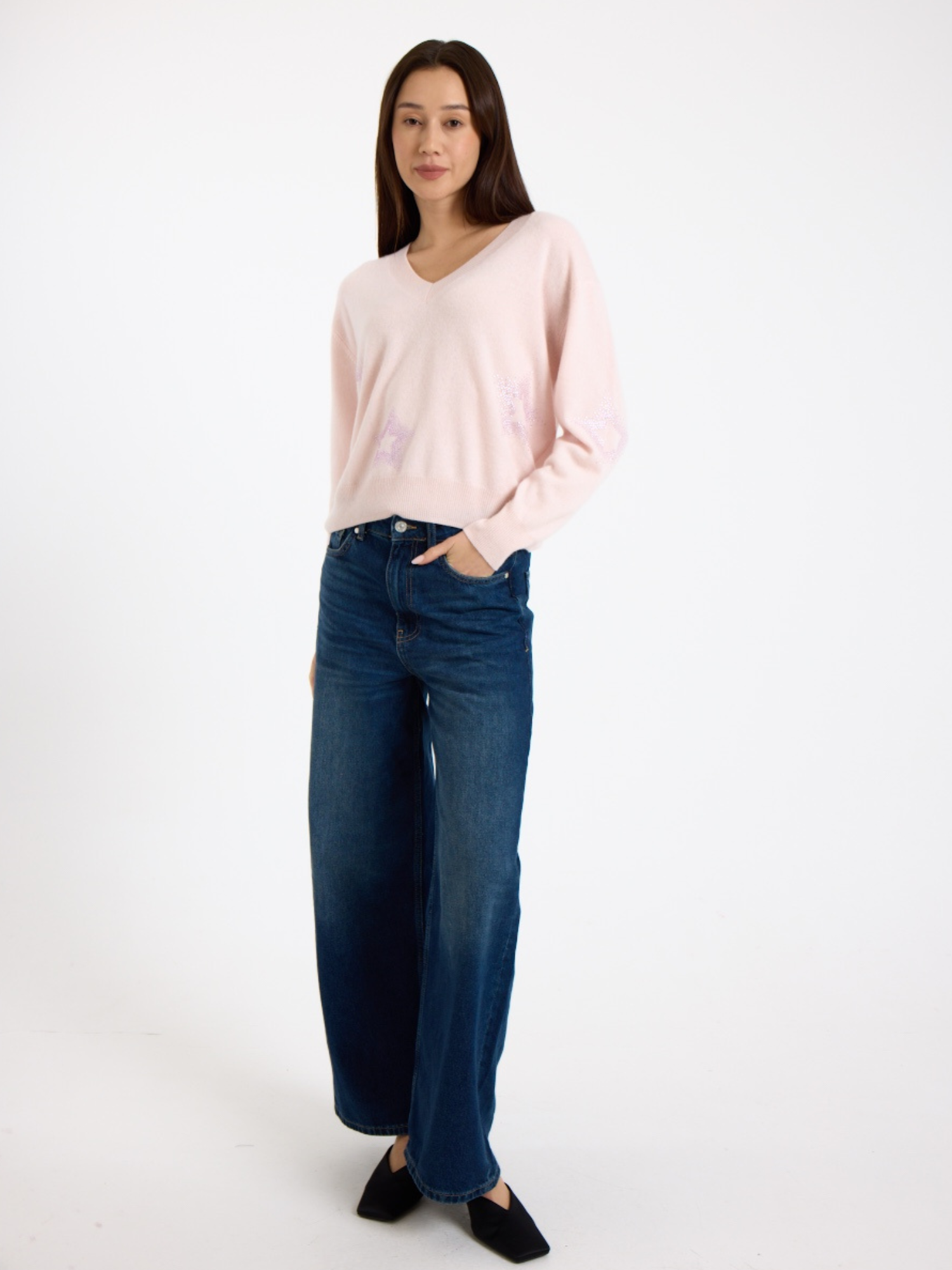 Woman wearing a light pink sweater with subtle star pattern and blue jeans on a white background
