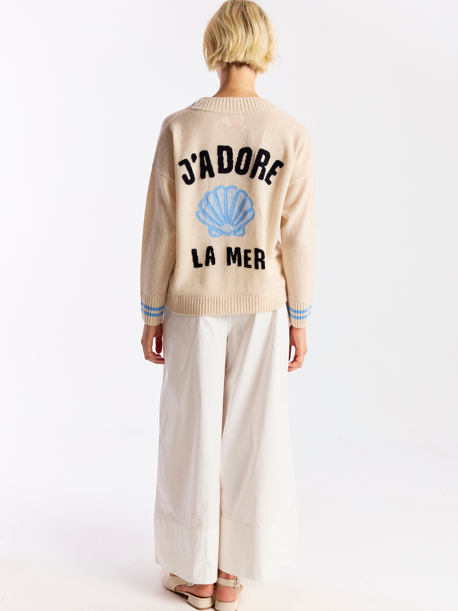 Person wearing a beige sweater with text and a shell design on a white background