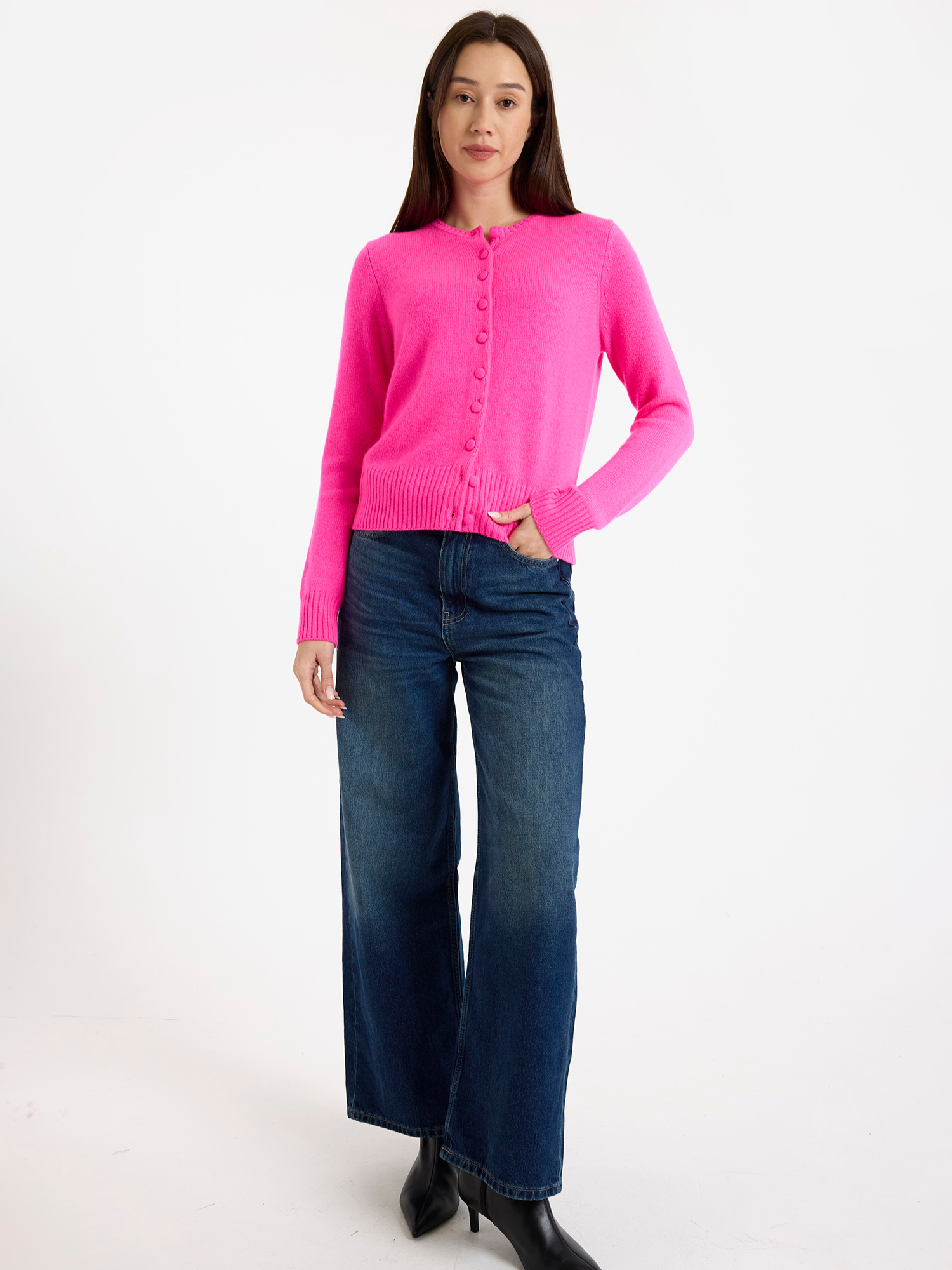 Woman wearing a bright pink cardigan and blue jeans on a white background