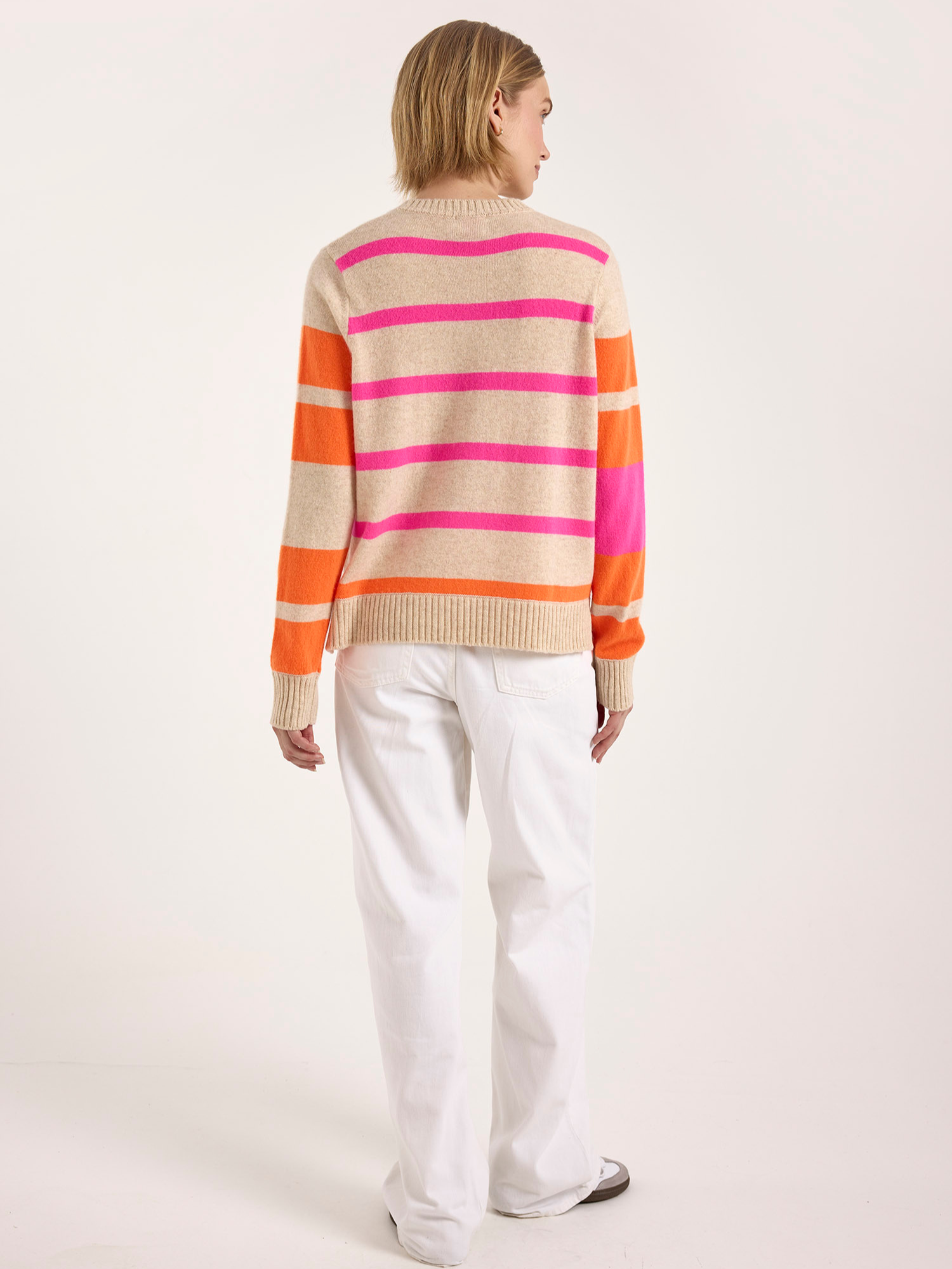 Woman wearing a beige cashmere sweater with pink and orange striped sleeves on a white background