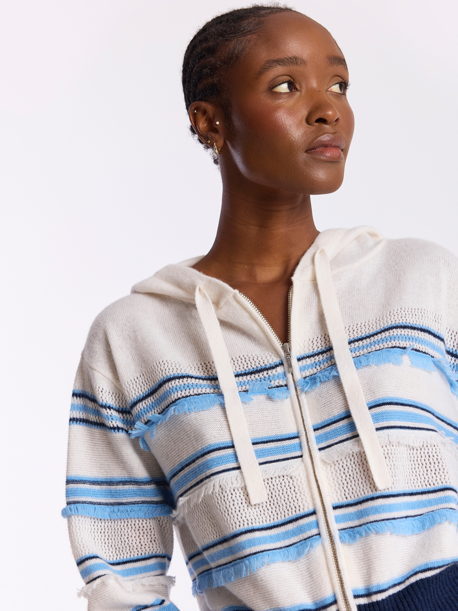 Woman wearing a white hoodie with blue stripes on a plain background