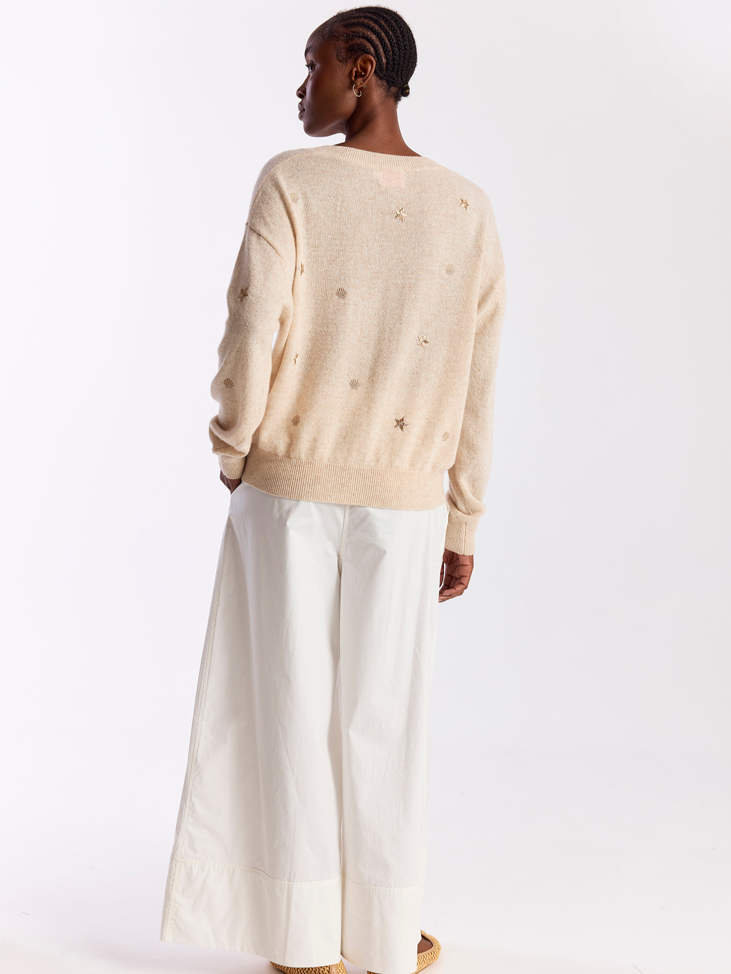 Person wearing a beige sweater and white pants on a white background