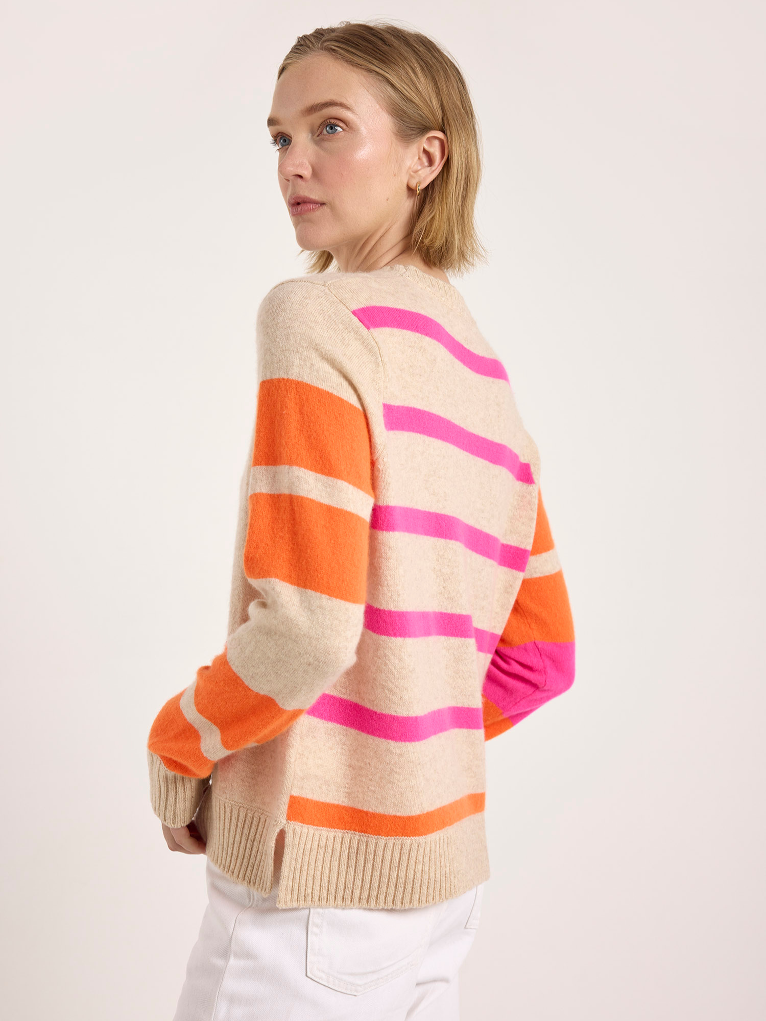 Woman wearing a beige cashmere sweater with pink and orange striped sleeves on a white background