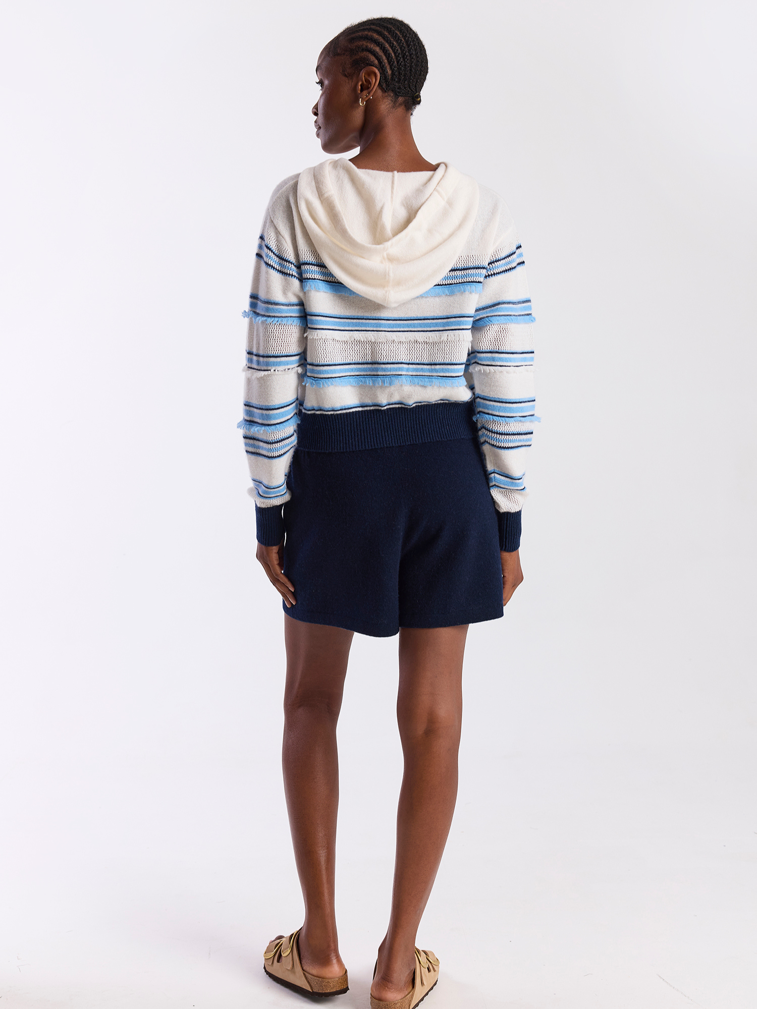 Person wearing a striped sweater and navy shorts on a white background