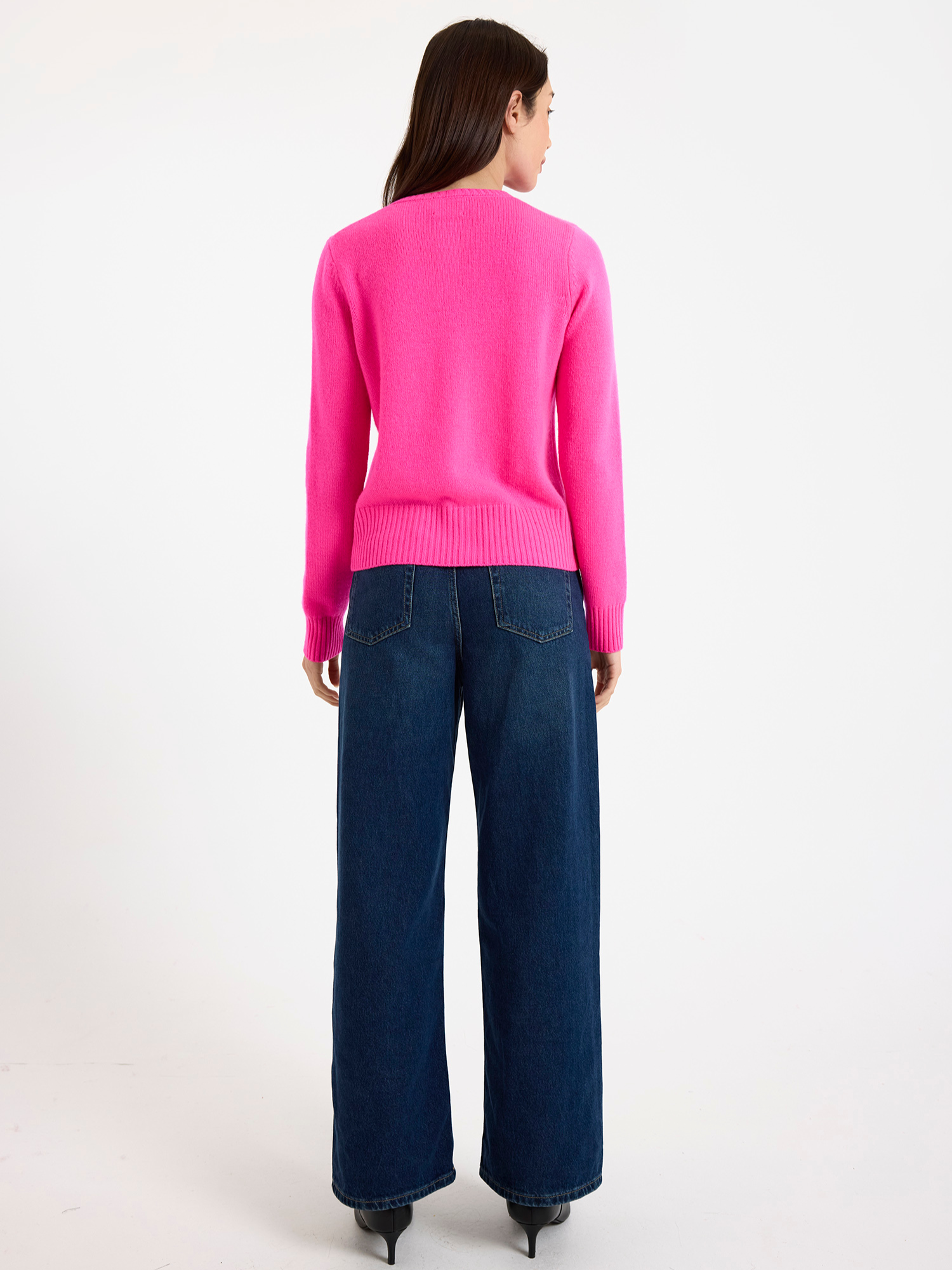 Woman wearing a bright cardigan and blue jeans on a white background