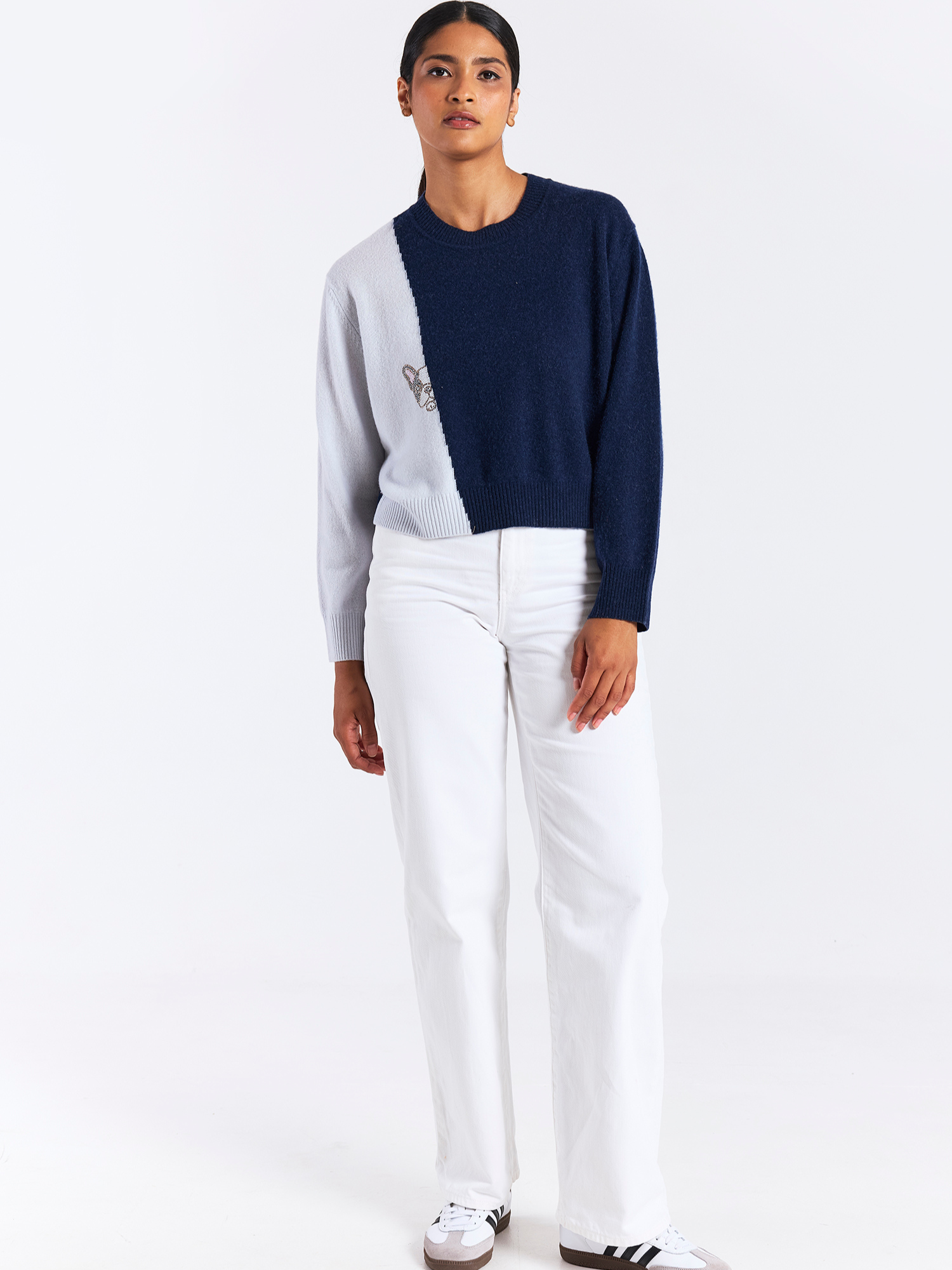 Person wearing a navy and white sweater with white pants on a white background