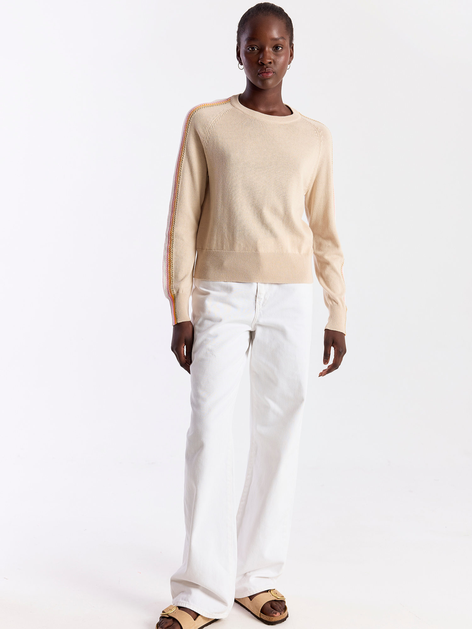 Person wearing a beige sweater and white pants on a white background