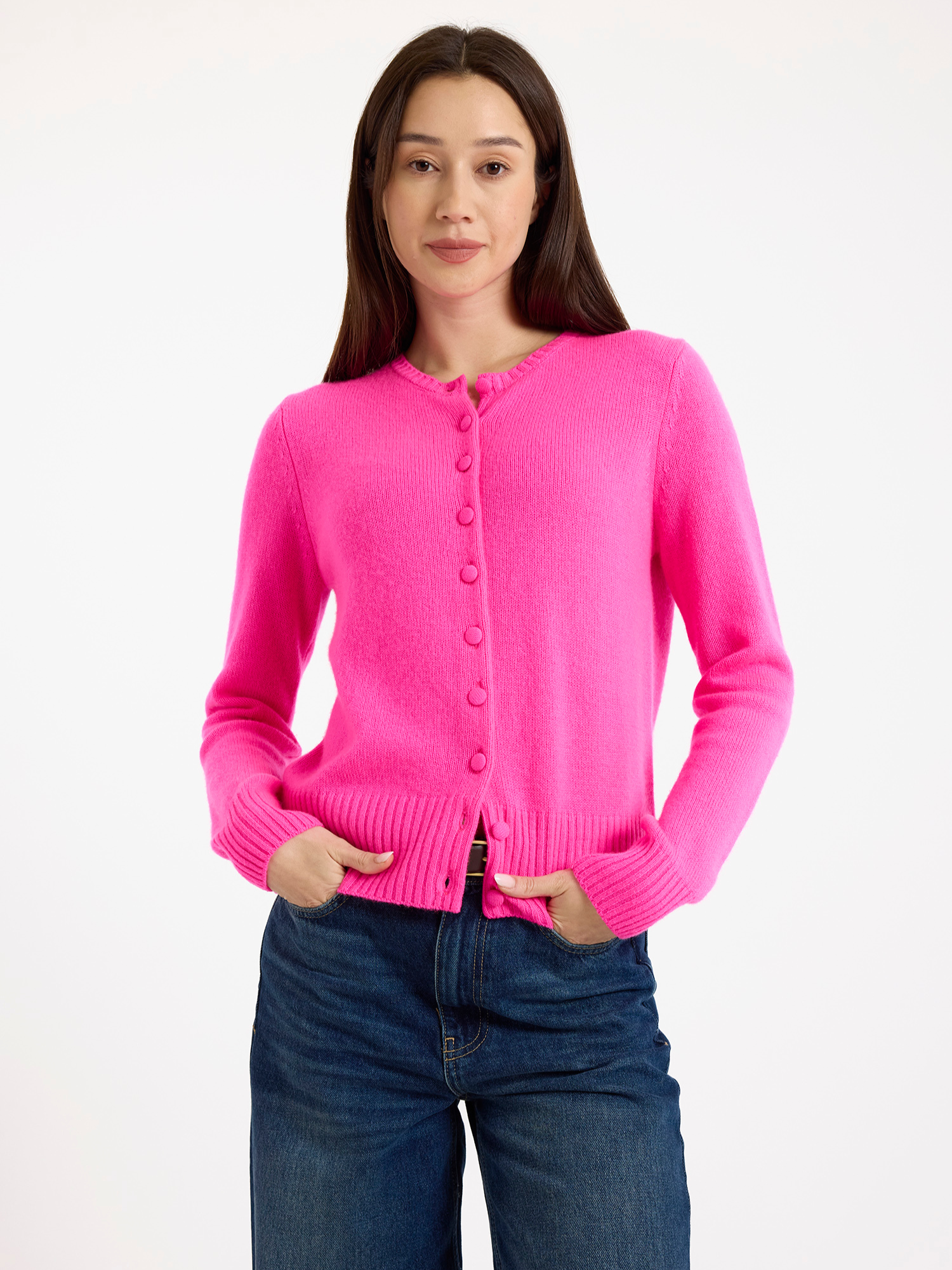 Woman wearing a bright pink cardigan and blue jeans on a white background