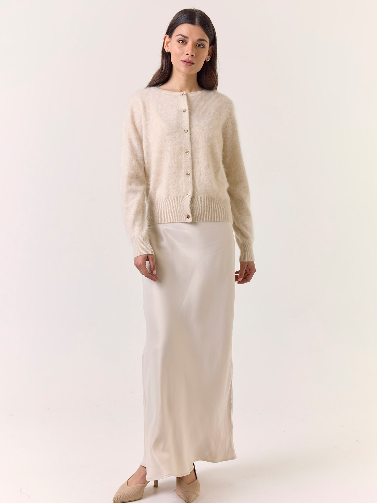 Woman wearing a beige cashmere cardigan and white skirt on a white background