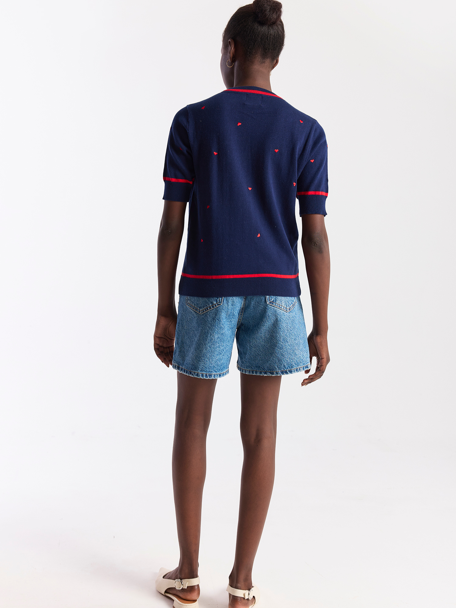 Person wearing a navy blue polo shirt with red accents and denim shorts on a white background